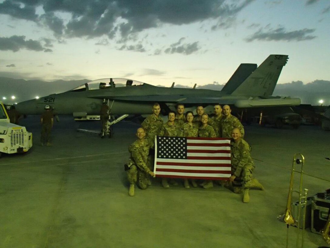 Rock Band members deployed to Afghanistan pose with a flag at Bagram Air Base.