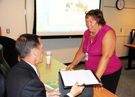 Valeria Mosqueira, assistant commander for Contracts at Marine Corps Systems Command, speaks to Shawn Reinwald, director of Marine Corps Programs at Cypress International, during the quarterly Industry Interface Council meeting Aug. 6 in Dumfries, Va. Marine Corps Systems Command hosted the event to discuss ways to improve communication between the command, PEO LS and industry partners. 
