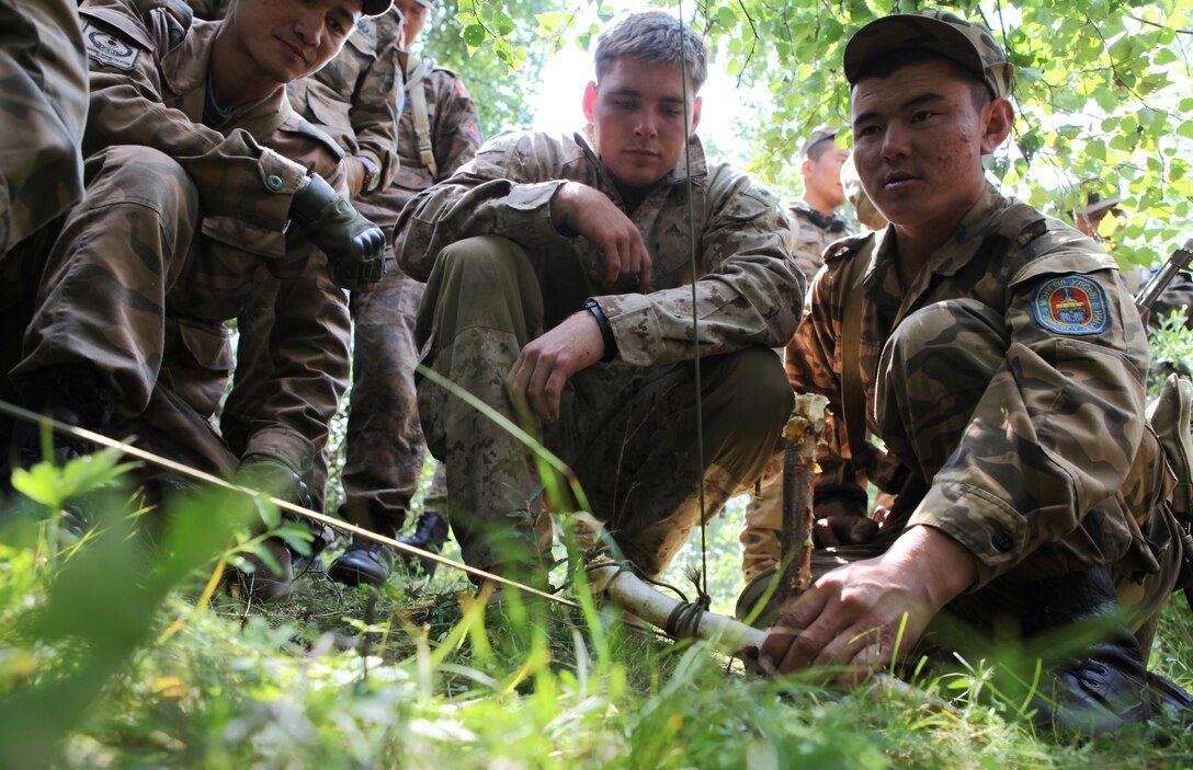 Sgt. Ts. Galmunkh, a member of the 065 Communication Unit, Mongolian Armed Forces, sets a trap while being observed by Cpl. Justin Haish, an instructor for the Khaan Quest 2013 survival course and assigned to the Jungle Warfare Training Center in Camp Gonsalves, Okinawa, Japan, Aug. 7. Khaan Quest is a peacekeeping operations-focused, combined training event between U.S. Marine Corps Forces Pacific, U.S. Army Pacific, and the MAF. MARFORPAC and USARPAC have conducted similar training with MAF since 2003, and this exercise marks the 11th iteration of Khaan Quest. Military personnel from Australia, Canada, France, Germany, Japan, India, Nepal, Republic of Korea, Tajikistan, United Kingdom and Vietnam are also participating in the exercise. Haish, currently part of the unit deployment program with Kilo Company, 3rd Battalion, 3rd Marine Regiment, is from Kailua, Hawaii.