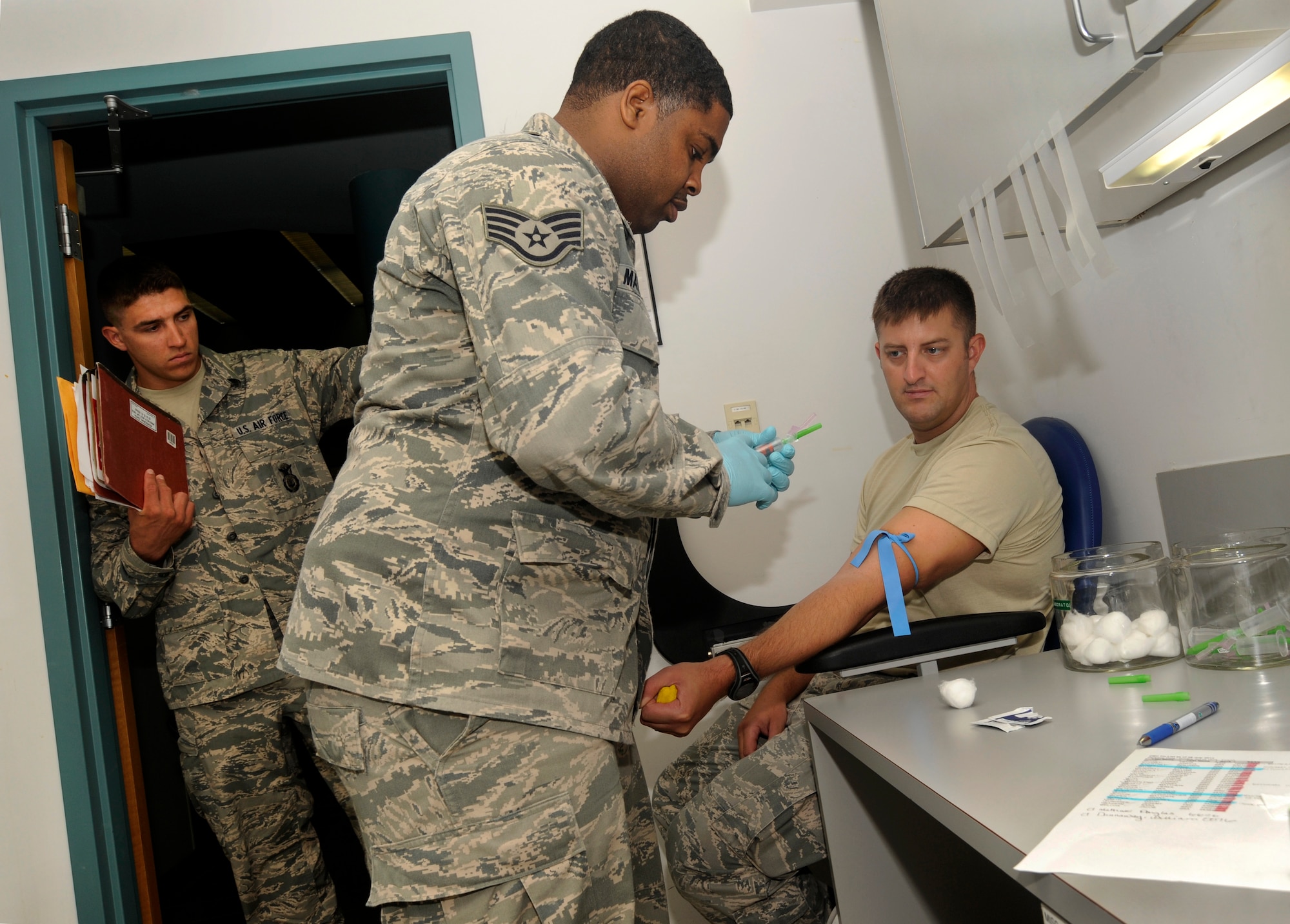 Oregon Air National Guard Staff Sgt. Clifton Matthews, 142nd Fighter Wing Medical Group, prepares to take a blood samples from Staff Sgt. Rockney Schock, (right) and Senior Airmen Benjamin Courtney (left), 142nd Fighter Wing Security Forces Squadron, as part of the in processing procedures at the Portland Air National Guard Base, Ore., Aug. 9, 2013.  (Air National Guard photo by Tech. Sgt. John Hughel, 142nd Fighter Wing Public Affairs/released)