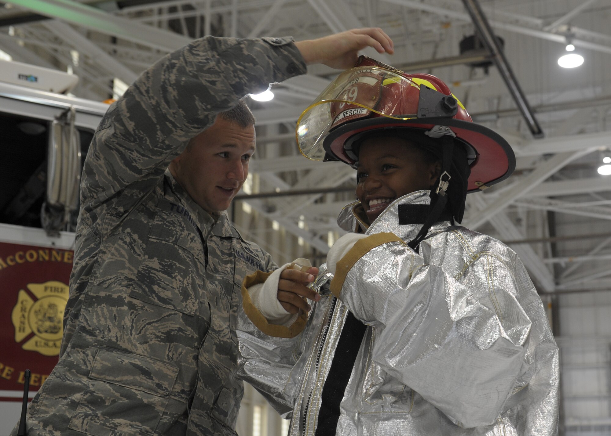 Staff Sgt. William Turner, 22nd Civil Engineer Squadron crew chief, places a fire helmet on Ivory, 11, during the 2013 Big for a Day event, Aug. 9, 2013, at McConnell Air Force Base, Kan. During the annual event, “Littles” were matched with Airmen “Bigs.” The children learned about the 22nd Air Refueling Wing’s while participating in various activities, including touring a KC-135 Stratotanker static display, watching a military working dog demonstration and donning fire protective gear. (U.S Air Force photo/Senior Airman Katrina M. Brisbin)