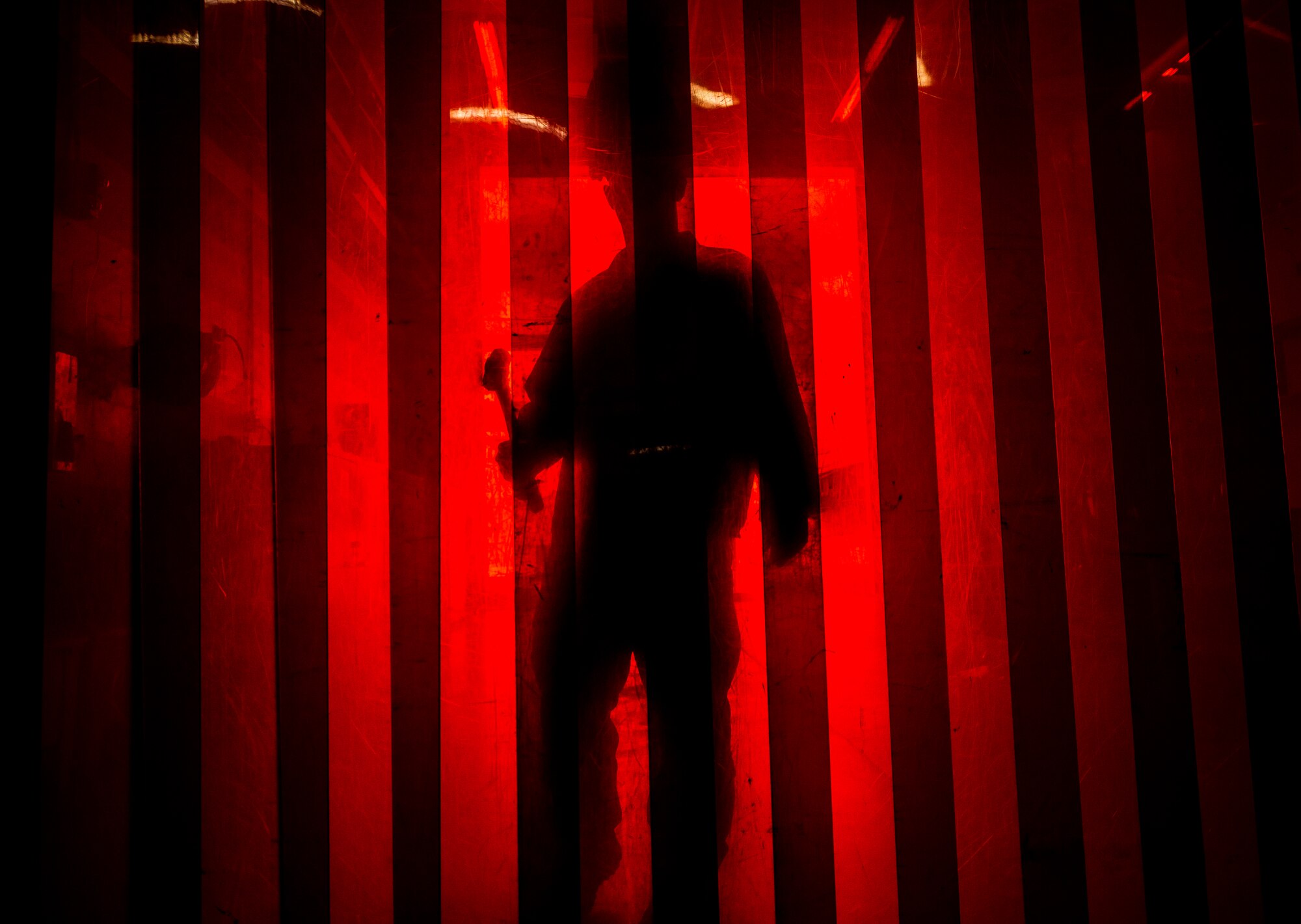 Master Sgt. Tim Thornton, 437th Maintenance Squadron aircraft metals shop noncommissioned officer in charge, walks towards arc welding protection drapes with a sledge hammer in his hands Aug. 7, 2013, at Joint Base Charleston, S.C. The red drapes protect individuals not wearing a welding shield from taking in the intense light emitted during welding produces. (U.S. Air Force photo/ Senior Airman Dennis Sloan)