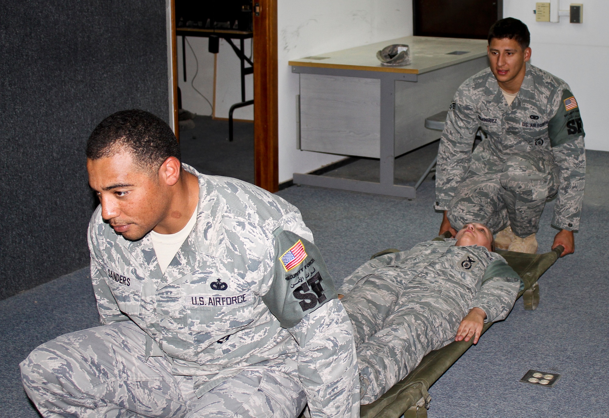 Staff Sgt. Jamal Sanders, left, and Senior Airman Luis Dominguez prepare to lift ‘patient’ Master Sgt. Candace Davis during a training exercise with local security personnel at the 64th Air Expeditionary Group in Southwest Asia, July 8, 2013. Eight members from the 64th AEG traveled to a local airport's security compound for integration training with 19 officers and enlisted members of the host nation's air forces. Sanders and Dominguez are 64th Expeditionary Security Forces Squadron operations members deployed from Tyndall Air Force Base, Fla., and the U. S. Air Force Academy respectively. Davis is the 64th ESFS training and evaluation section chief deployed from Eielson AFB, Alaska. (Courtesy photo)