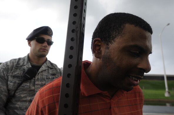 Staff Sgt. Che Mason, (foreground) of the 436th Aerial Port Squadron, leans against a sign post while being held by Senior Airman Sean Shields, 436th Security Forces Squadron, after being taken in to custody during a Major Accident Response Exercise, August 12, 2013, Dover Air Force Base, Del. Mason played the role of an armed-robber during a simulated test of security and response times by the Security forces personnel as part of the MARE. (U.S. Air Force photo/Greg L. Davis)