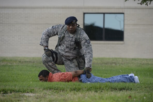 Technical Sgt. Laurance Isaac, 436th Security Forces Squadron, pats down Staff Sgt. Che Mason, 436th Aerial Port Squadron, who is playing the role of a robber during a simulated armed-robbery at building 520, Dover Air Force Base, Del. on August 12, 2013. The simulated armed robbery is one of many scenarios taking place as part of a Major Accident Response Exercise from August 12-14. (U.S. Air Force photo/Greg L. Davis)
