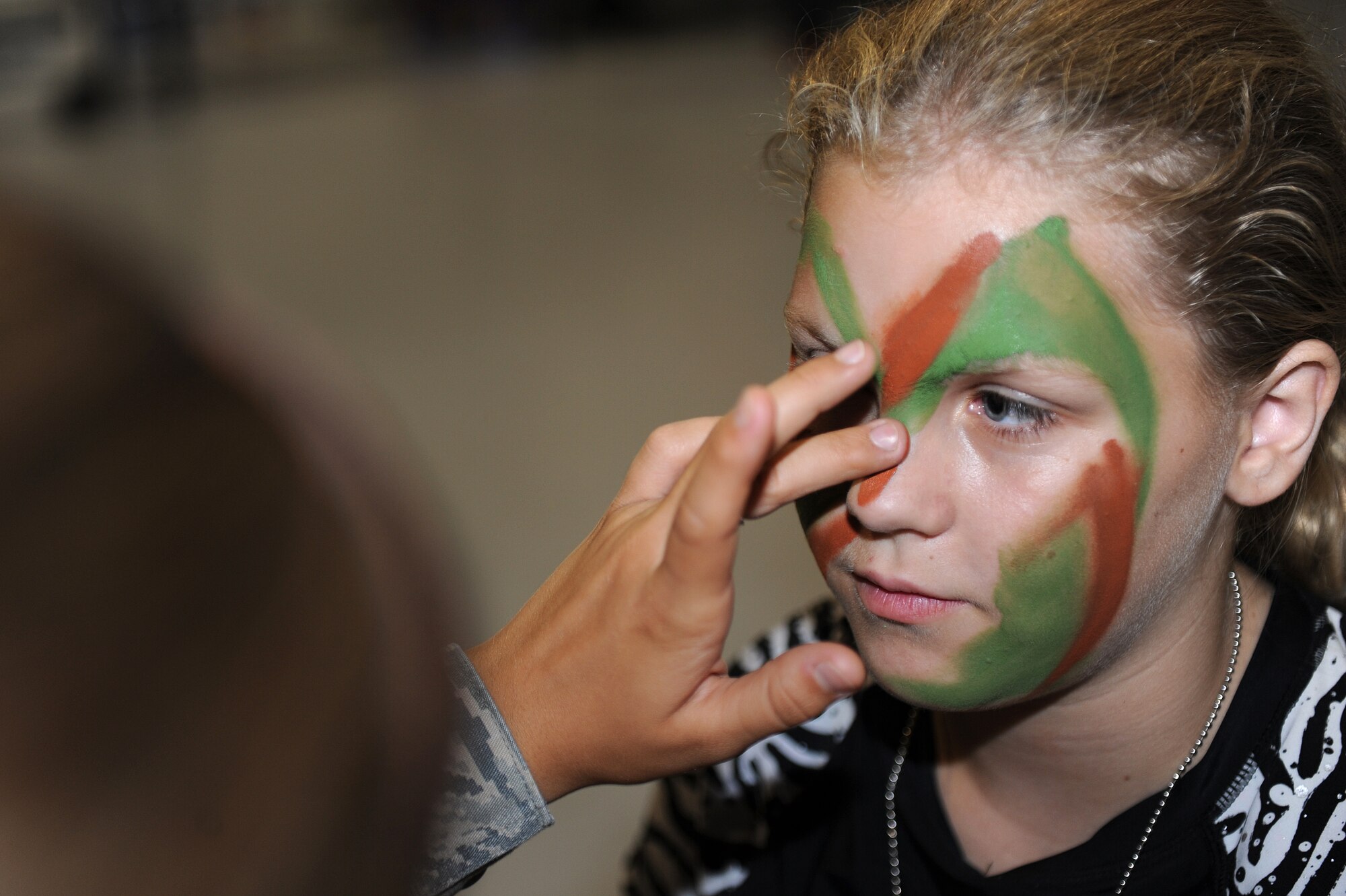 A volunteer applies camouflage-patterned paint to Kaylee Jenkins’ face during Operation Hero at Langley Air Force Base, Va., Aug. 7, 2013. Some of the event’s activities included explosive ordnance disposal simulations and a meals, ready to eat (MRE) tasting station. (U.S. Air Force photo by Airman 1st Class Kimberly Nagle/Released) 
 
