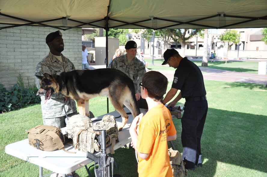 Staff Sgt. Lindsey Thompson, left, 56th Security Forces Squadron Military Working Dog handler, and Wax, 56th SFS MWD, interact with a local resident during the annual Dog Days of Summer event held Saturday in Glendale. This year’s event focused on public service dogs and their importance in the community. (U.S. Air Force photo/Staff Sgt. Luther Mitchell)