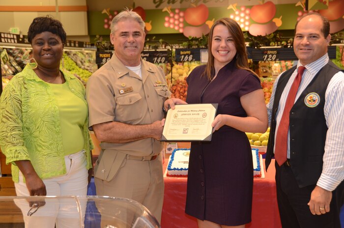 JOINT BASE CHARLESTON - WEAPONS STATION, S.C. — Naval Support Activity Charleston Commanding Officer Capt. Timothy Sparks, Earlene Mills, Weapons Station commissary store manager and Thomas Mundinger, assistant store director present the Scholarship for Military Children to Jennifer Bailey, daughter of JB Charleston deputy commander Navy Capt. Thomas Bailey and Janet at the Weapons Station commissary Aug. 1, 2013. The $1,500 scholarship is one way the Defense Commissary Agency and Fisher House contribute back to the military community. (U.S. Navy photo/ Petty Officer 1st Class Chad Hallford)