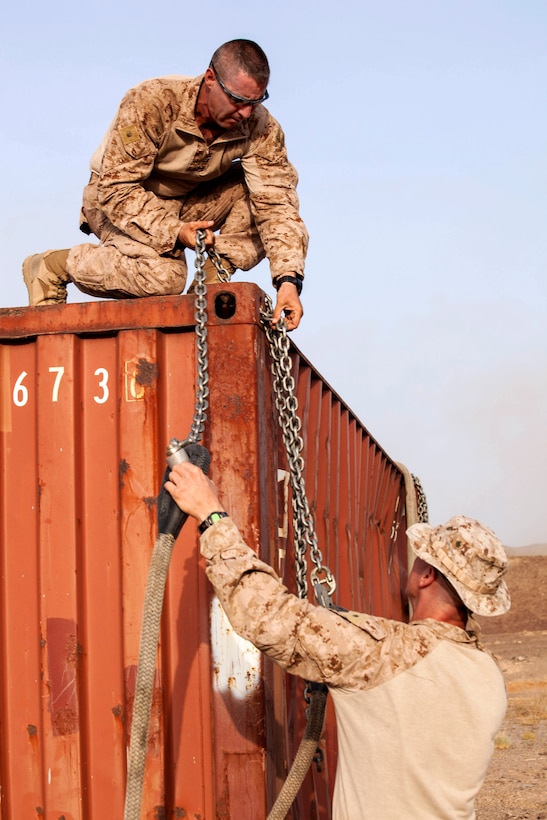 U.S. Marine Corps Lt. Col. Kevin G. Collins, bottom right, and U.S. Marine Corps Maj. Kenneth Morrow, top, unhook a transport harness from a shipping container that will be used as a training target on a range in Djibouti, August 2, 2013. Collins is commander of the Combat Logistics Battalion 26, 26th Marine Expeditionary Unit, and Morrow, an assistant air officer, is assigned to the 26th Marine Expeditionary Unit.