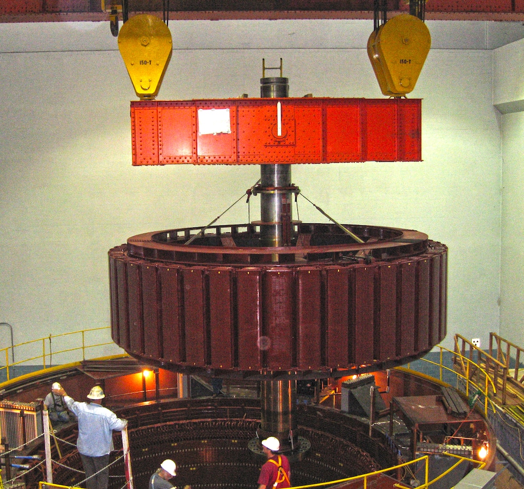 Overhead bridge cranes travel the interior length of Corps powerhouses, mounted on parallel rails above the huge generators. A hoist, the lifting component of a crane, travels across the width of the bridge crane carrying loads and suspending multi-ton parts for maintenance and installation projects.
This is a smaller bridge crane, with a capacity of 300 tons; shown here as it “flies a load” in Detroit Dam’s powerhouse.