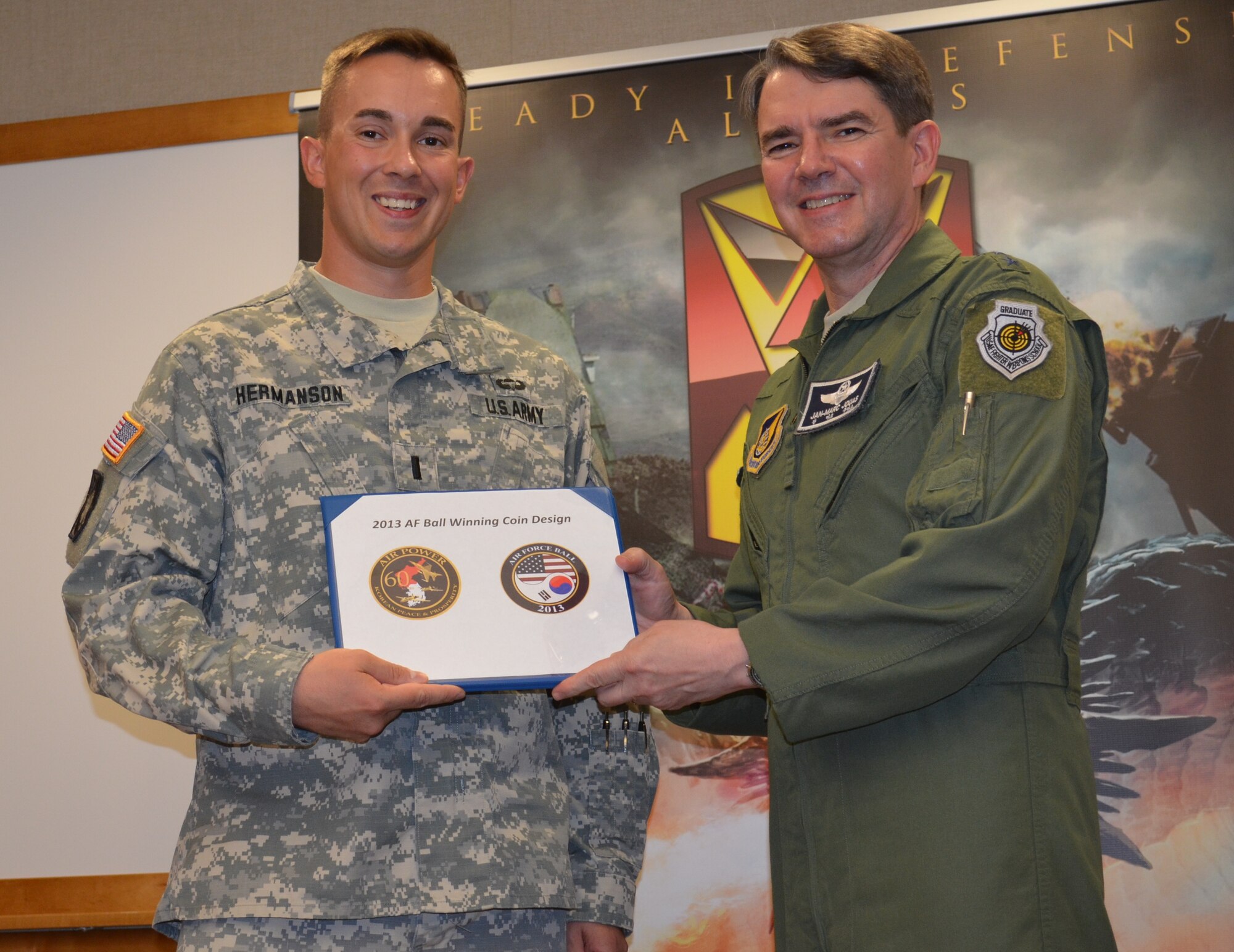 Lt. Gen.  Jan-Marc Jouas, commander of the 7th Air Force at Osan Air Base, poses with the winning coin design with 1st Lt.  Kyle Hermanson, executive officer with Battery B, 6th Battalion, 52nd Air Defense Artillery Regiment at Osan Air Base, Aug. 9. Hermanson is married to Allison Hermanson, a flight medic with the Air Force Individual Ready Reserve.  They are expecting their first child at the end of September. (U.S. Army Photo By Spc. Shawn Denham, PAO, 35th ADA.)
