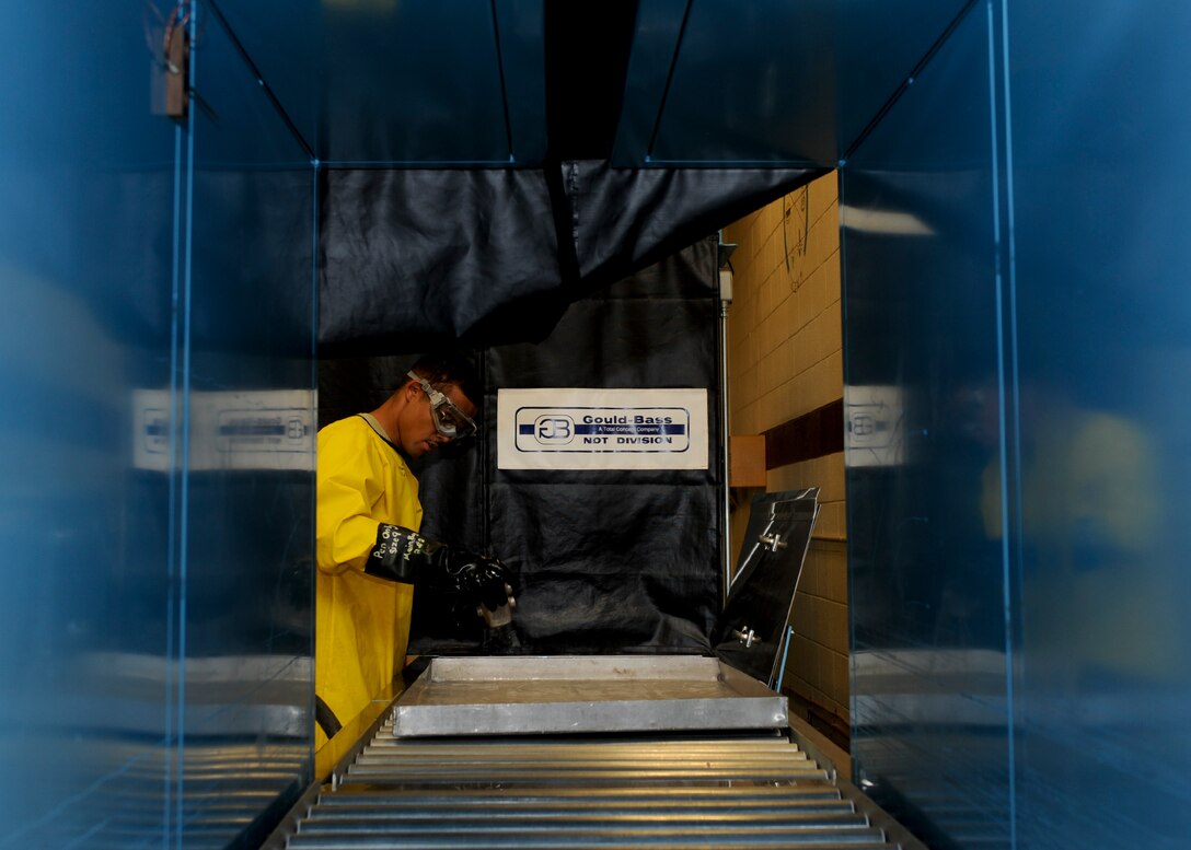Airman 1st Class Charles Mills, 28th Maintenance Squadron nondestructive inspection technician, rinses hydrophilic remover from a hydraulic accumulator piece at Ellsworth Air Force Base, S.D., Aug. 9, 2013. After the part is thoroughly rinsed, it will go through the developer stage where water suspended powder is applied, pulling penetrant from the cracks to enhance visual inspection when finally examined under black lights. (U.S. Air Force photo by Airman 1st Class Anania Tekurio/Released)