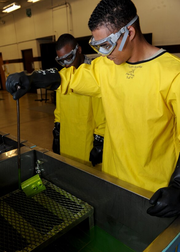 Airman 1st Class Charles Mills and Shane Gorman, 28th Maintenance Squadron nondestructive inspection technicians, remove a hydraulic accumulator out of penetrant liquid during inspection at Ellsworth Air Force Base, S.D., Aug. 9, 2013.  It is vital to let the penetrant liquid completely absorb into the piece for 30 minutes to 4 hours, allowing for proper visual inspection to take place afterwards. (U.S. Air Force photo by Airman 1st Class Anania Tekurio/Released))