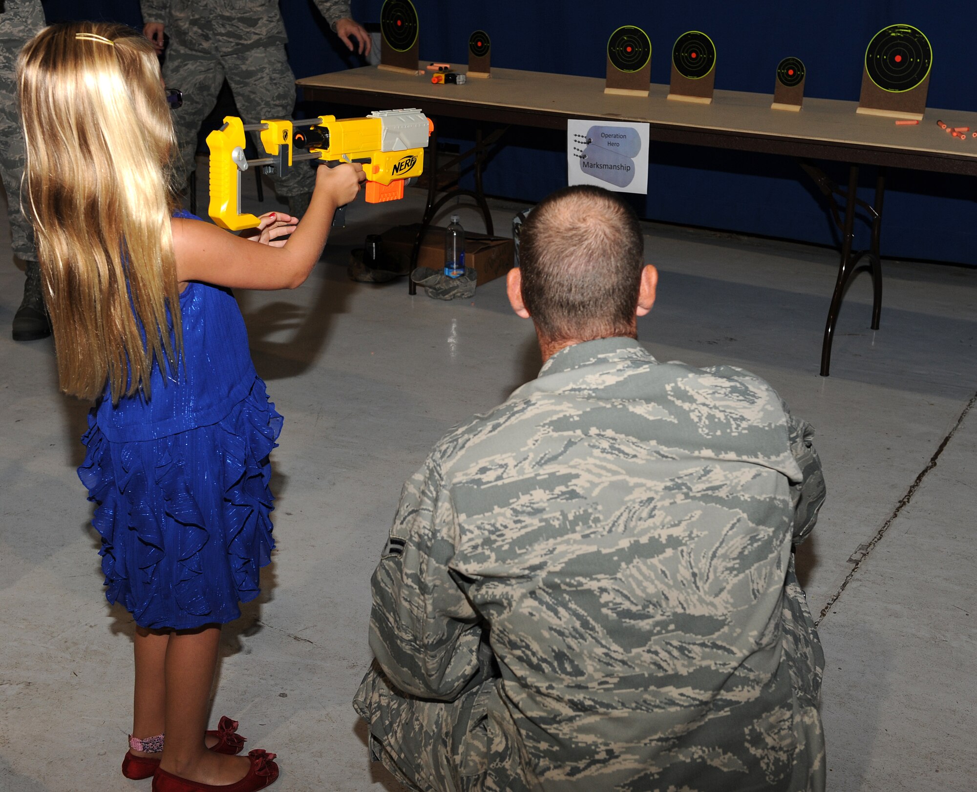 U.S. Air Force Airman 1st Class Carlton, 10th Intelligence Squadron technician, assists Anne Percivalle at a marksmanship station during the annual Operation Hero event at Langley Air Force Base, Va., Aug. 7, 2013. Carlton was one of many Airmen who volunteered during the event to educate children on deployments. (U.S. Air Force photo by Senior Airman Brittany Paerschke-O’Brien/Released) (Last name withheld for security reasons)