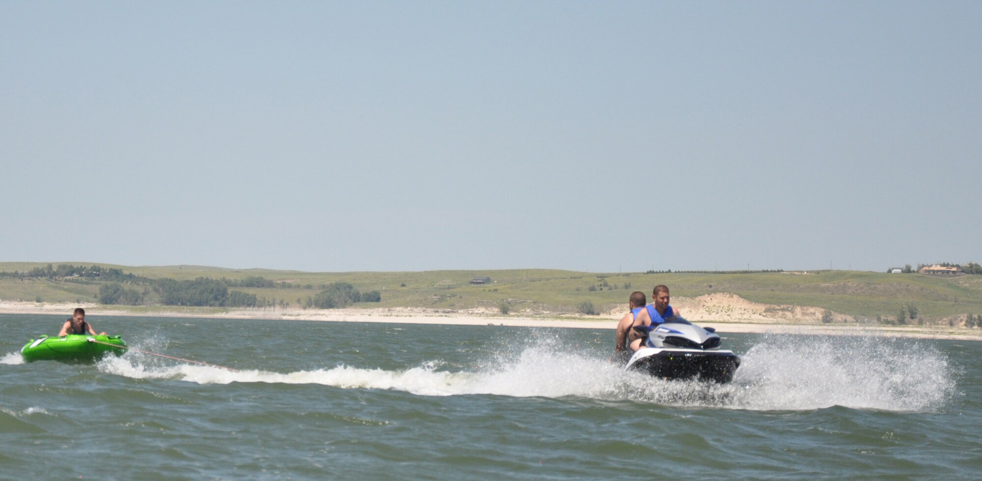 130810-F-GZ967-178 Brandon Valle and Kyle Holt ride a Jet Ski while pulling Tyler Young on an inflatable tube on Lake McConaughy, Neb. The group spent a three-day weekend trip out on the lake through Outdoor Recreation’s Single Airmen Adventure Program.