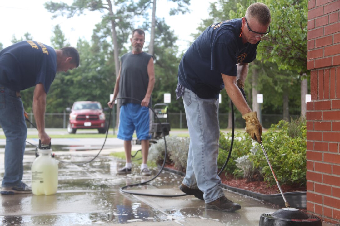 Chief Petty Officer Michael P. Larson (left), a supply chief with Headquarters and Headquarters Squadron, local volunteer Frank Butin (center) and Chief Petty Officer Rich W. Hubbard (right), an air medical safety corpsman with the 2nd Marine Aircraft Wing, cleans a concrete pathway at Graham A. Barden Elementary School Friday. 