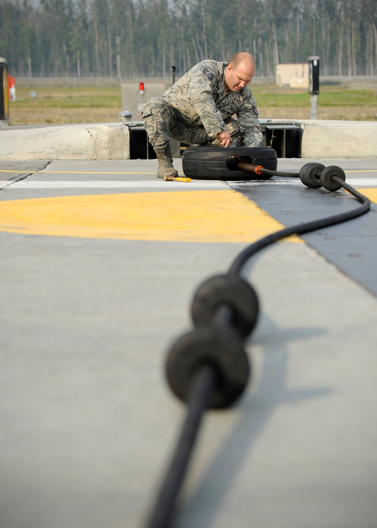 Tech. Sgt. Brian Brown, 354th Civil Engineer Squadron power production NCO in charge, adjusts a disk system, which connects a 1.25 inch cable to a six-inch thick, 1,600 feet long nylon strap on the flight line during RED FLAG-Alaska 13-3 Aug. 14, 2013, Eielson Air Force Base, Alaska. The cable system is used in case of an emergency landing when an aircraft needs to make an abrupt stop. (U.S. Air Force photo by Senior Airman Shawn Nickel/Released)
