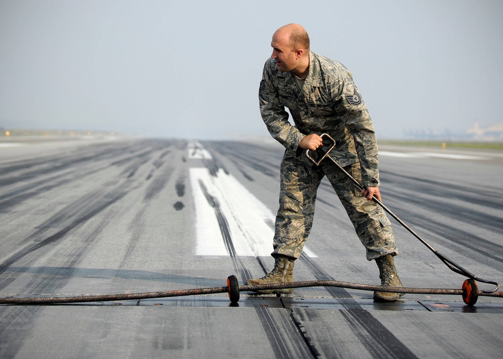 Tech. Sgt. Brian Brown, 354th Civil Engineer Squadron power production NCO in charge, drags a cable into place in preparation for an aircraft landing during RED FLAG-Alaska 13-3 Aug. 14, 2013, Eielson Air Force Base, Alaska. Brown compares the cable stop to the braking system on an aircraft carrier where planes risk going into the sea if they aren’t stopped.  (U.S. Air Force photo by Senior Airman Shawn Nickel/Released)