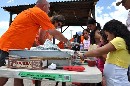 U.S. Army Lt. Col. Russell Cote, Medical Element deputy commander, and Rebecca Veliz,  410th Contracting Support Brigade civilian contract officer, serve hot dogs and hamburgers to children during Fiesta Day here Aug. 10, 2013. The JTF-Bravo’s MEDEL joined with “Kick for Nick,” a nonprofit organization, to hold a Fiesta Day, during the event, more than 75 girls from a local orphanage received more than 35 soccer balls donated by the organization, while also participating in other activities. (Photo released by U.S. Air Force Staff Sgt. Jarrod Chavana)