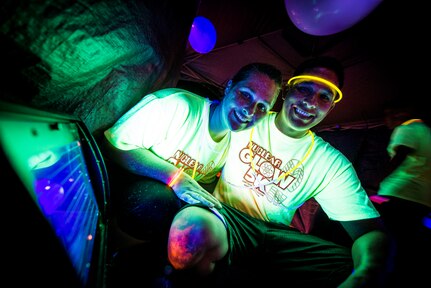 Petty Officer 1st Class Adam Sanchez, Nuclear Power Training Unit instructor, and his wife Melissa, are illuminated by an ultraviolet light in a tent after the Nuclear Glow 5K Aug. 9, 2013, at Joint Base Charleston – Weapons Station, S.C. Service members and their families ran through base housing wearing glow-in-the-dark-clothing and accessories. (U.S. Air Force photo/ Senior Airman Dennis Sloan)