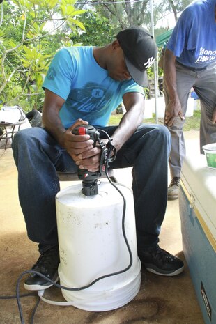 Lance Cpl. Austin J. Gilbert, Marine Aircraft Group 12 aviation electronics specialist, drills a hole in the bottom of a bucket during the Island Girl Power community relations project July 27, 2013. Island Girl Power rewarded the volunteers by feeding them after the project was complete. 