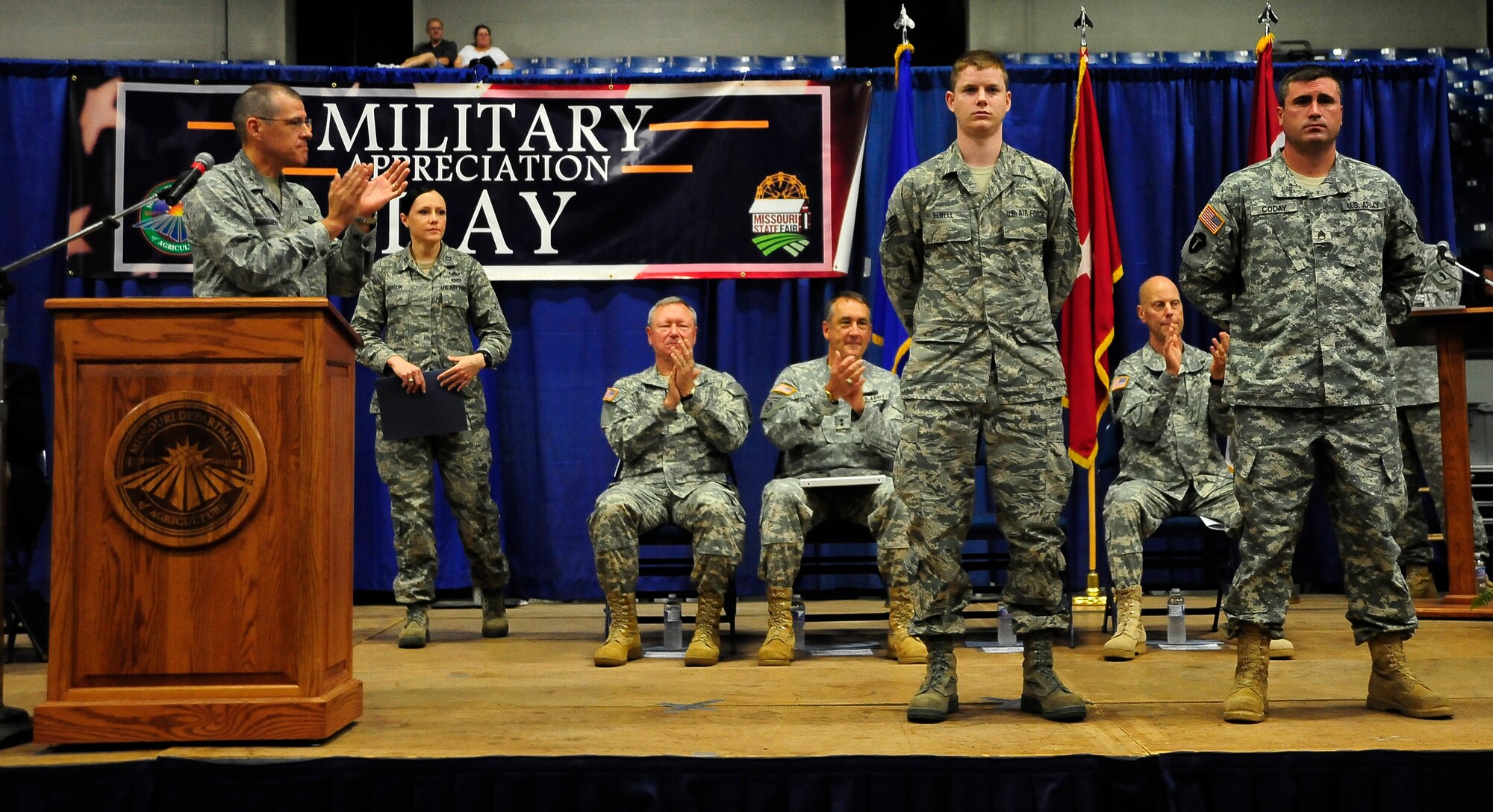 U.S. Air Force Brig. Gen. Thomas Bussiere, left, 509th Bomb Wing commander, applauds the efforts of Missouri Air National Guard Staff Sgt. Joseph Elwell, center, 131st Operations Support Flight intelligence analyst, and Missouri Army National Guard Staff Sgt. Ryan Coday, 1st Battalion, 135th Aviation Regiment, Aug. 11, 2013, at the Missouri State Fair in Sedalia, Mo. Bussiere spoke to the crowd about the importance of the close working relationship between the 509th BW Airmen and the National Guardsmen stationed at Whiteman Air Force Base. (U.S. Air Force photo by Staff Sgt. Brigitte N. Brantley/Released)