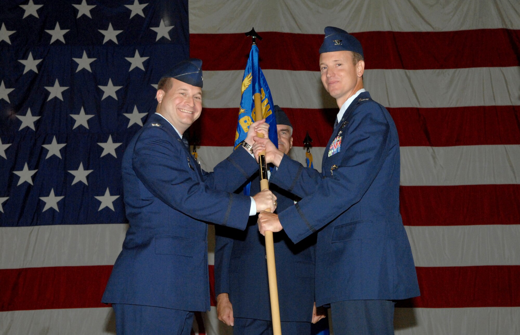 (At left) Col. Phillip A. Stewart, 9th Reconnaissance Wing commander, hands off the 69th Reconnaissance Group guidon to Col. Lawrence Spinetta during a change of command ceremony Aug. 14, 2013, at the 3 Bay hangar on Grand Forks Air Force Base, N.D. Spinetta replaced Col. J. Scott Winstead, who recently retired from active duty after 26 years of service. (U.S. Air Force photo/Staff Sgt. Susan Davis)