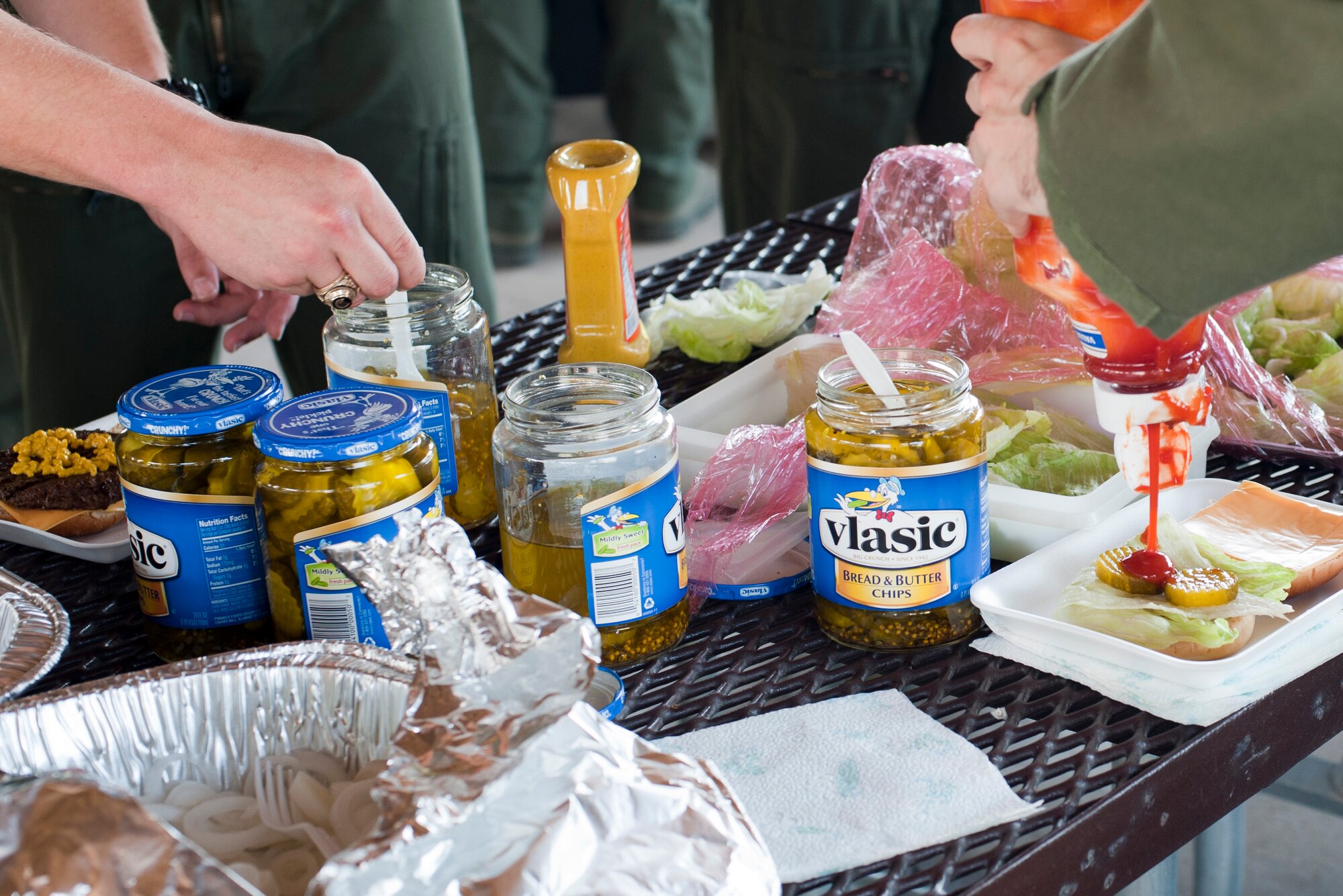 Patrons of the burger burn fundraiser prepare their burgers at the gazebo behind the Student Squadron building here, Aug. 16, 2013. Canned food could be brought for a small discount towards the meal which included a burger, chips and a drink. (U.S. Air Force photo/Airman 1st Class Jimmie D. Pike)