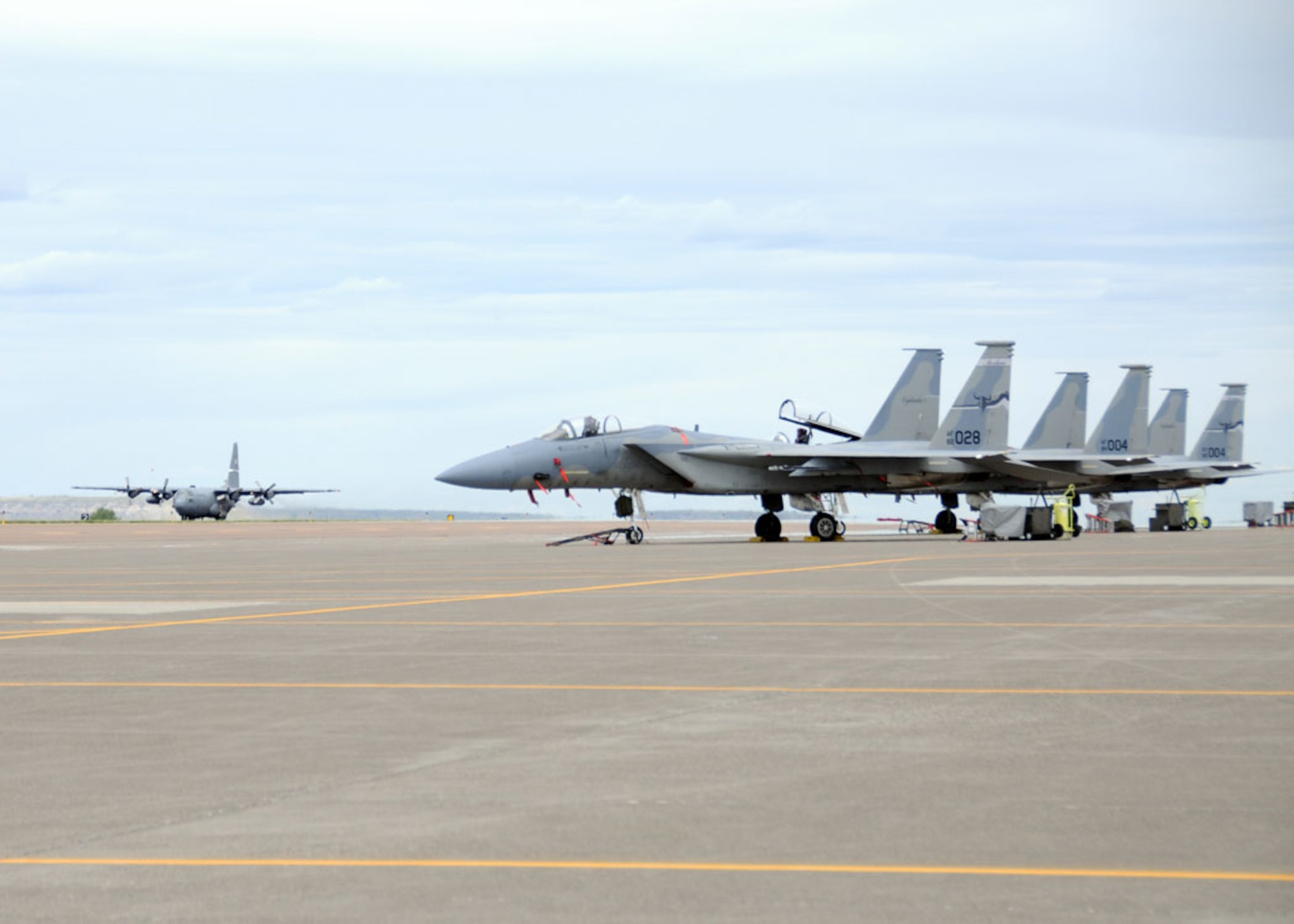 A C-130 Hercules transport aircraft assigned to the Kentucky Air National Guard taxis toward F-15 Eagle fighter aircraft parked on the ramp of the 120th Fighter Wing on June 1, 2012. (U.S. Air Force photo/Senior Master Sgt. Eric Peterson)