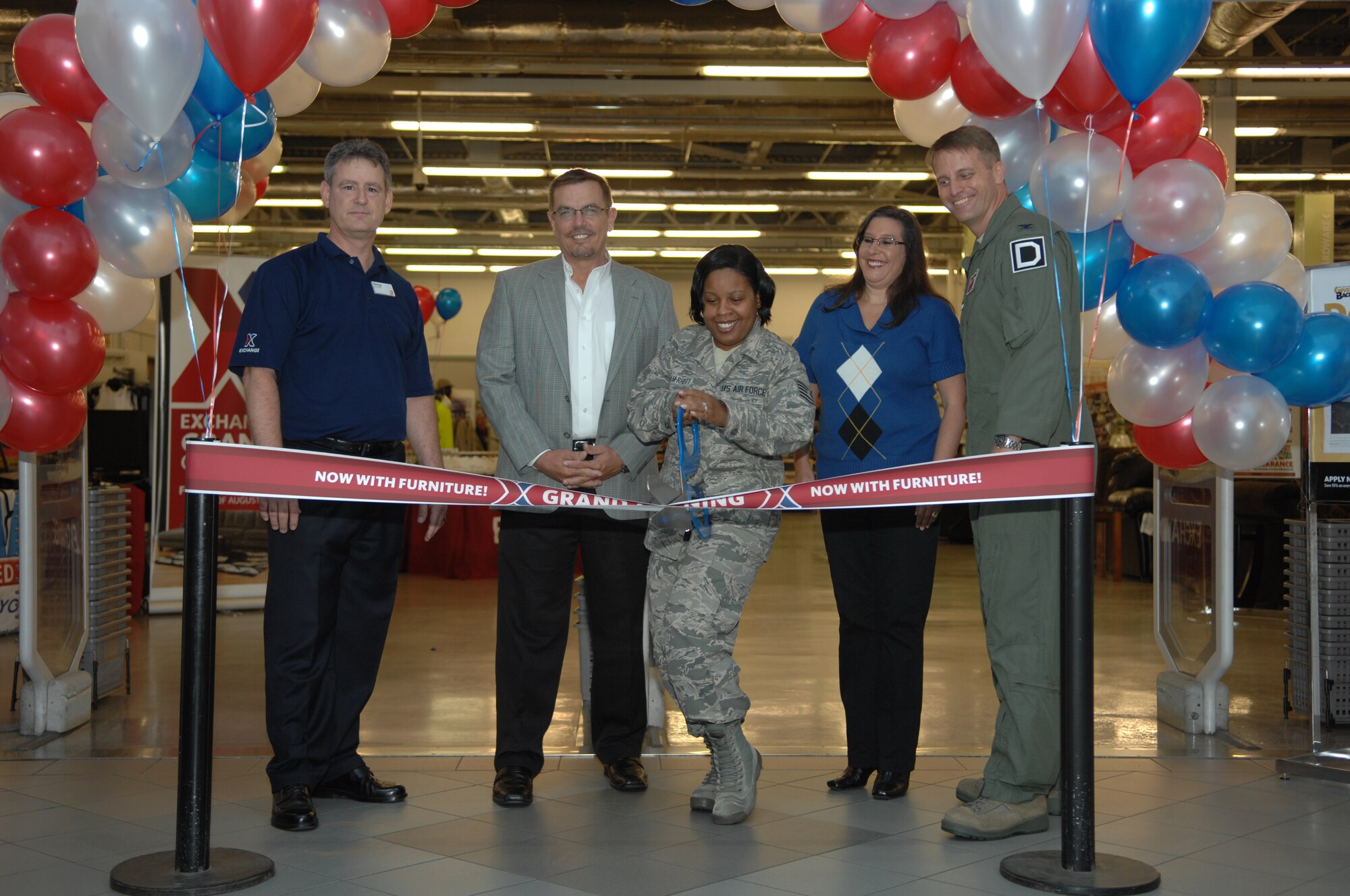 U.S. Air Force Tech. Sgt. April Dunham-Rhett, 100th Air Refueling Wing Equal Opportunity advisor from Macon, Ga., cuts the ribbon during the BXtra furniture store grand opening Aug. 16, 2013, on RAF Mildenhall, England. The furniture store moved from RAF Feltwell to RAF Mildenhall to better serve the military members who shop there. The grand opening included a ribbon cutting and complimentary cake and beverages. (U.S. Air Force photo by Airman 1st Class Dillon Johnston/Released) 