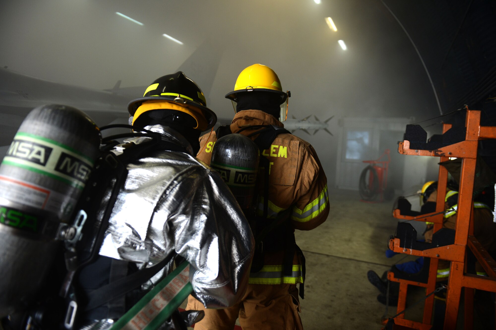 SPANGDAHLEM AIR BASE, Germany – U.S. Air Force Staff Sgt. Jessica Crotta, 52nd Civil Engineer Squadron crew chief from Palatine, Ill., left, and U.S. Air Force Airman 1st Class Daniel Prokowich, 52nd CES fire protection technician carry a fire hose in to a hardened aircraft shelter during an aircraft fire training exercise Aug. 14, 2013. Firefighters learn to proceed into these situations in a sweeping motion from one corner to another to be sure all potential victims are found with such low visibility. (U.S. Air Force photo by Airman 1st Class Gustavo Castillo/Released) 