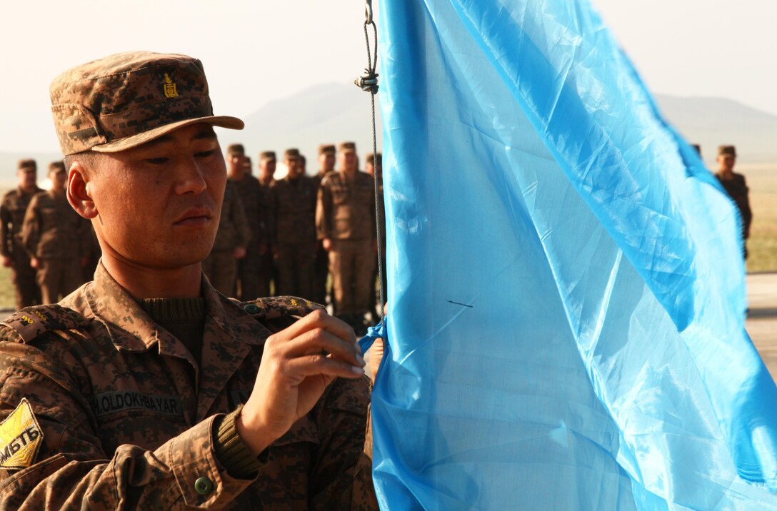 Junior Sgt. Sh. Oldokhbayar, Peace Support Operations Training Center, Mongolian Armed Forces, prepares to raise a banner prior to the opening ceremony for the Non-Lethal Weapons Executive Seminar at Five Hills Training Area, Mongolia, Aug. 17. NOLES is a regularly scheduled field training exercise and leadership seminar sponsored by U.S. Marine Corps Forces Pacific, and hosted annually by various nations throughout Asia-Pacific. In its 12th iteration, this multinational training event is designed to promote awareness and effective use of non-lethal weapons as a tool to maintain order in low-intensity conflict situations or during incidents of civil unrest. Mongolia, a regular participant, is hosting NOLES for the third time. 