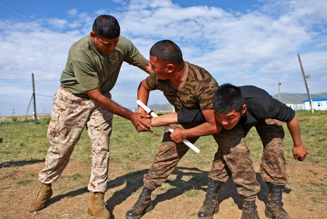 Sgt. Patrick Garza, a non-lethal weapons instructor with 3rd Law Enforcement Battalion, 3rd Marine Expeditionary Force Headquarters Group, III MEF, adjusts the positioning of a Mongolian Armed Forces service member while rehearsing baton techniques at Five Hills Training Area, Mongolia, Aug. 19. The drills took place during the field training portion of the Non-Lethal Weapons Executive Seminar, a regularly scheduled field training exercise and leadership seminar sponsored by U.S. Marine Corps Forces Pacific, and hosted annually by various nations throughout Asia-Pacific. In its 12th iteration, this multinational training event is designed to promote awareness and effective use of non-lethal weapons. Mongolia, a regular participant, is hosting NOLES for the third time. Garza is from Dallas.