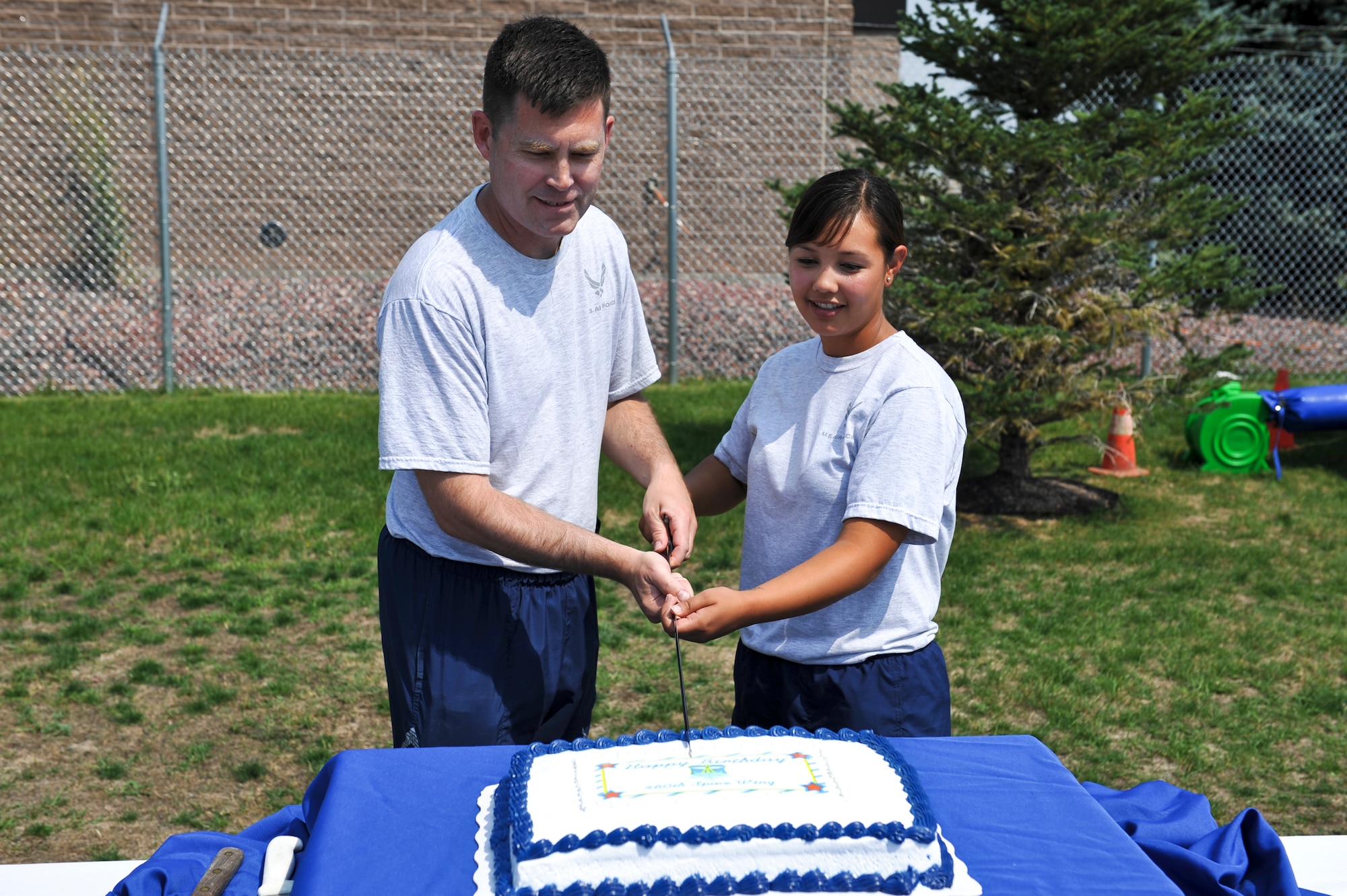 Col. Dan Wright, 460th Space Wing commander, and Airman Amanda Belarde, 460th SW Legal Office paralegal, cut a birthday cake at Fun Fest Aug. 16, 2013, at the softball fields on Buckley Air Force Base, Colo. Belarde was chosen to cut the cake because she is the Airman with the least amount of time-in-service assigned to the 460th SW. (U.S. Air Force photo by Airman 1st Class Riley Johnson/Released)