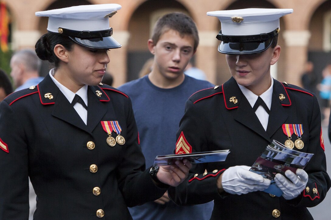 Pfc. Lucero Rodriguez, left, and Cpl. Katia Benefiel, right, both hosters with Marine Barracks Washington, D.C., organize parade programs during a Friday Evening Parade at the Barracks Aug. 16. 