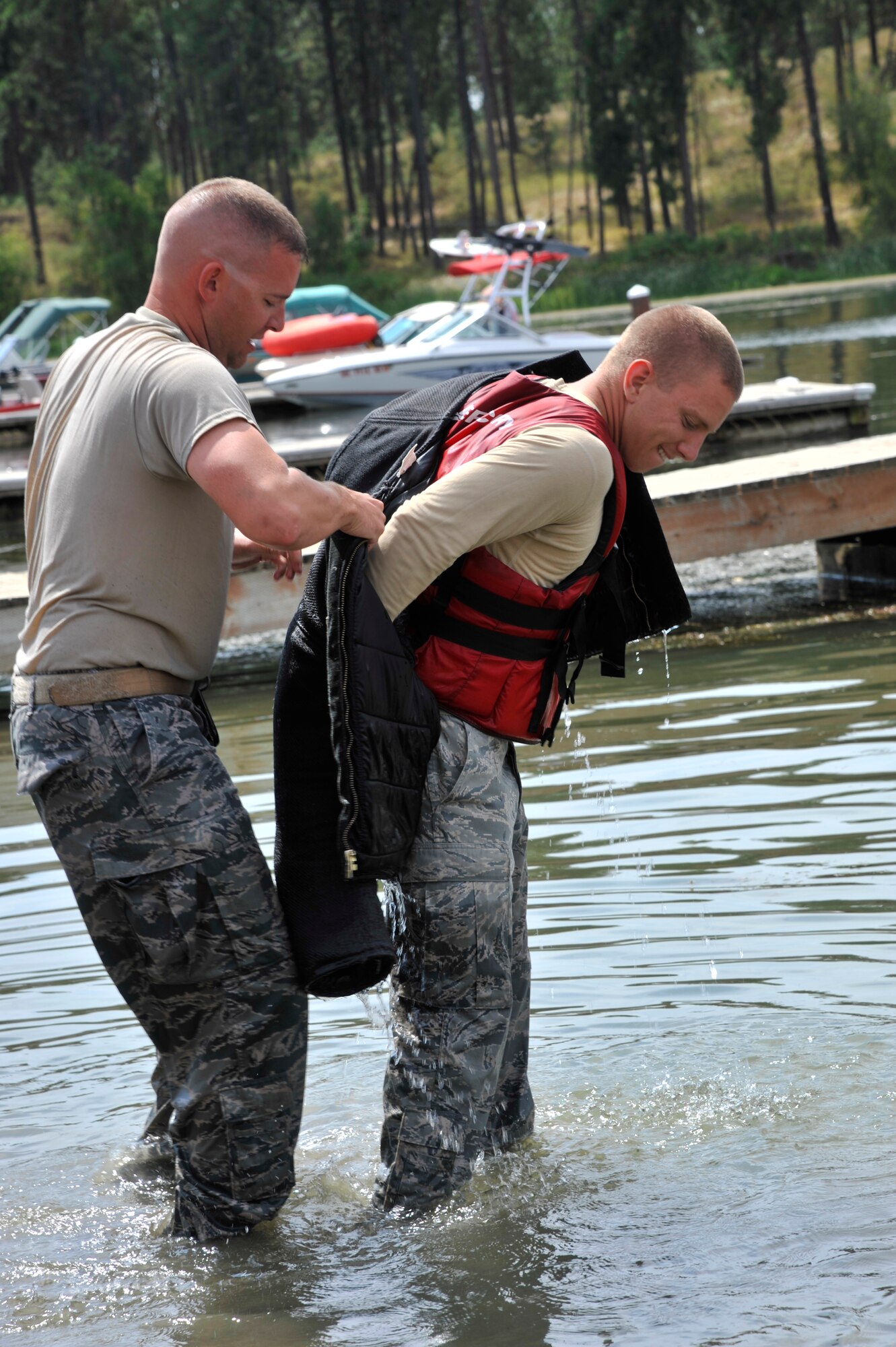 Staff Sgt. Brett Meyers helps Tech. Sgt. Thomas Winn put on protective gear during bite training at Clear Lake Resort in Cheney, Wash., Aug. 16, 2013. Meyers and Winn are both 92nd Security Forces Squadron military working dog handlers at Fairchild Air Force Base, Wash. (U.S. Air Force photo by Senior Airman Mary O'Dell/Released)