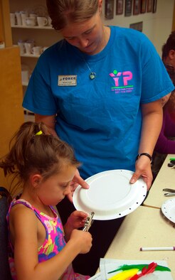 130813-F-GZ967-033 Hannah Cooper, Child and Youth Programs Assistant and music, art, and theater teacher at the Youth Center here, helps Chelsea Singbury begin working on her “deerskin” shield. Cooper was the chaperone from the Child and Youth Center who helped the Arts and Crafts Center youth camp as they explored the history of Wyoming. (U.S. Air Force photo by Airman 1st Class Brandon Valle)