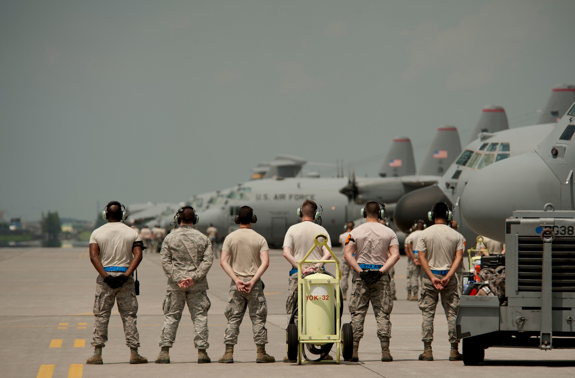 A group of maintainers stand at ease while seven C-130 Hercules spin up before taking to the air during a large formation mission at Yokota Air Base, Japan, Aug. 19, 2013. The aircraft flew in formation practicing airlift tactics and procedures. (U.S. Air Force photo by Senior Airman Michael Washburn)