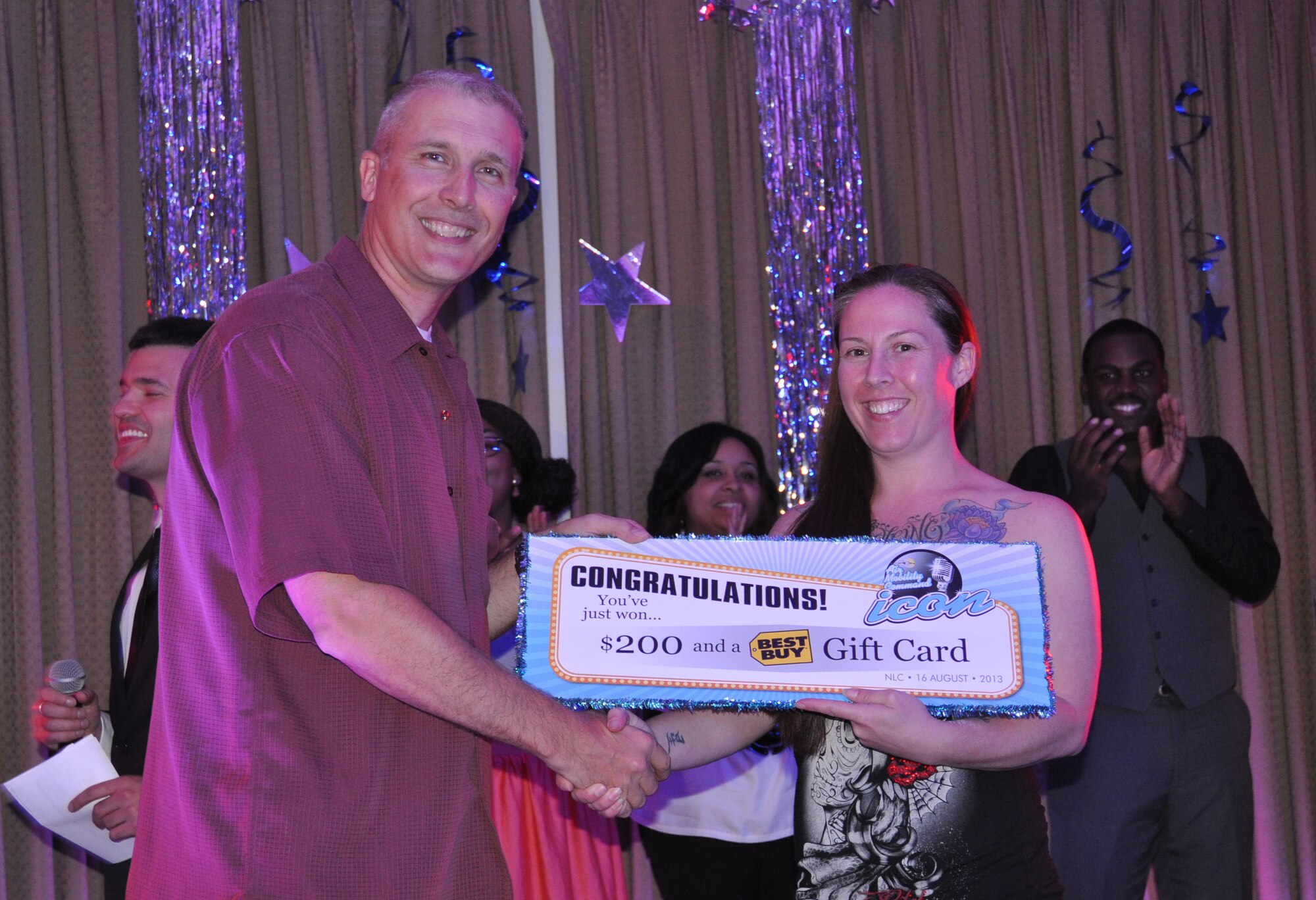 Col. Paul Bauman, 319th Air Base Wing commander, presents Tech. Sgt. Mindy Tyson with a congratulatory poster for $200 and a $50 Best Buy gift card for placing third at this year’s Air Mobility Command Icon base-level singing competition, which took place Aug. 16, 2013 at the Northern Lights Club on Grand Forks Air Force Base, N.D.  Tyson took third place with her performance of, "Killing Them Softly" by the Fugees. To view more photos of this Year’s contest, visit http://www.forksupport.com/extras/IconPhotos.html. (U.S. Air Force photo/Julie McWalter)
