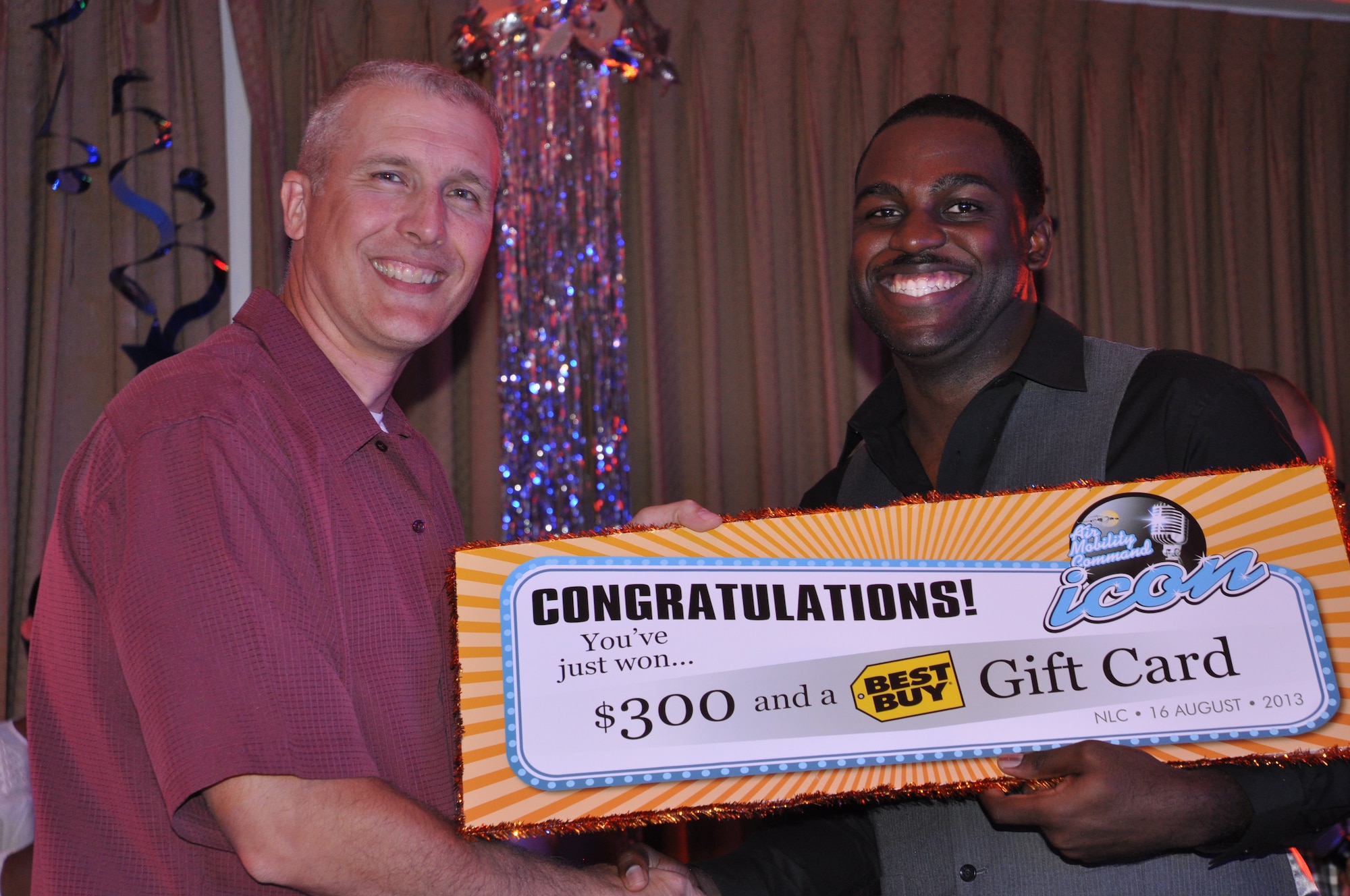 Col. Paul Bauman, 319th Air Base Wing commander, presents Airman 1st Class Andrew Hicks with a congratulatory poster for $300 and a $75 Best Buy gift card for placing second at this year’s Air Mobility Command Icon base-level singing competition, which took place Aug. 16, 2013 at the Northern Lights Club on Grand Forks Air Force Base, N.D. Hicks performed his rendition of the soul music hit, "This is a Man's World" by James Brown. He was the top placing active-duty member and will compete for the AMC-wide title later this fall. To view more photos of this Year’s contest, visit http://www.forksupport.com/extras/IconPhotos.html. (U.S. Air Force photo/Julie McWalter)