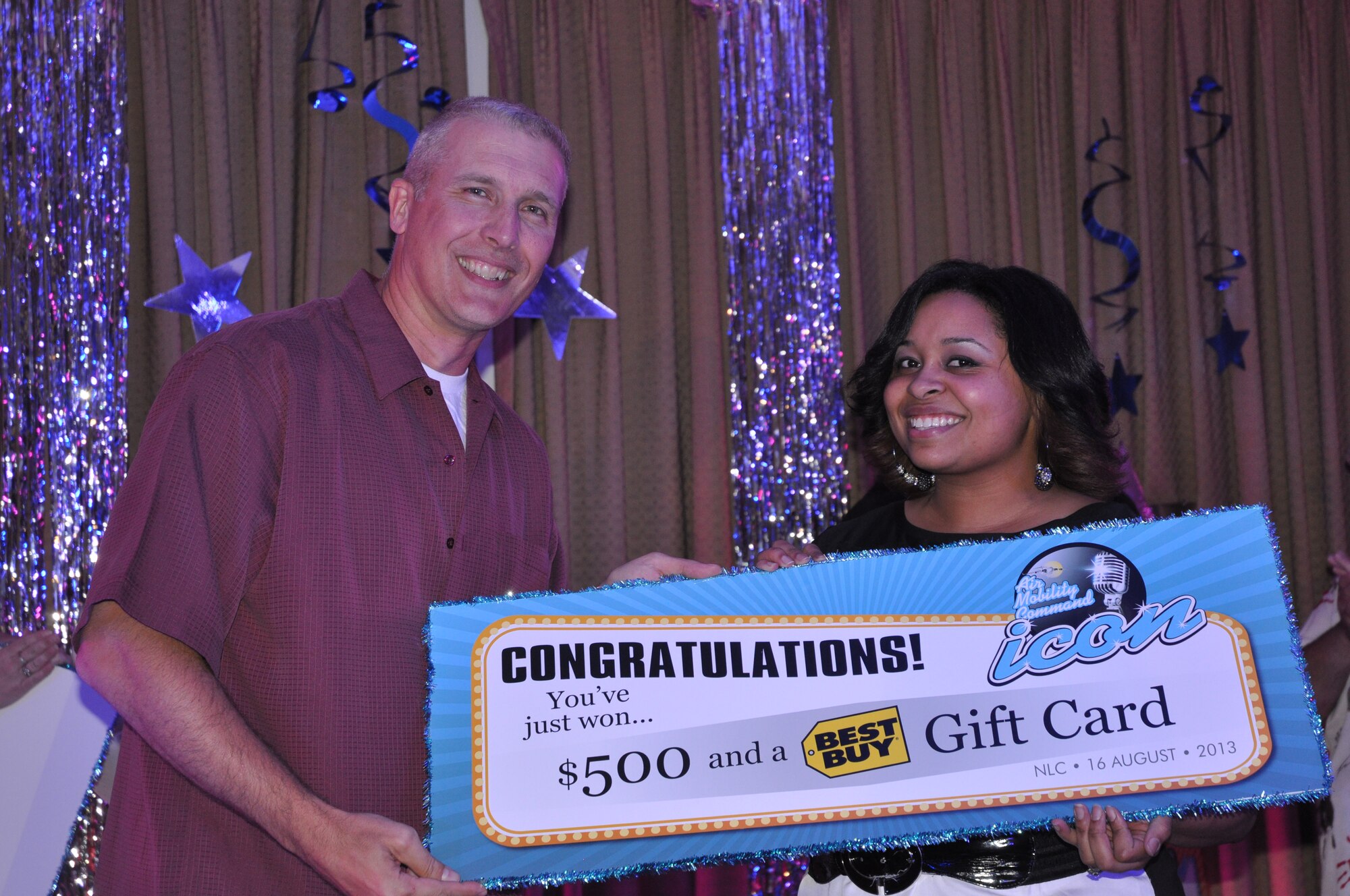 Col. Paul Bauman, 319th Air Base Wing commander, presents Sophie Shanks with a congratulatory poster for $500 cash and a $100 Best Buy gift card for placing first at this year’s AMC Icon local competition, which took place Aug. 16, 2013 at the Northern Lights Club on Grand Forks Air Force Base, N.D. Shanks won the Air Mobility Command’s base-level singing competition with her rendition of Stevie Wonder's, "All I Do." To view more photos of this Year’s contest, visit http://www.forksupport.com/extras/IconPhotos.html. (U.S. Air Force photo/Julie McWalter)