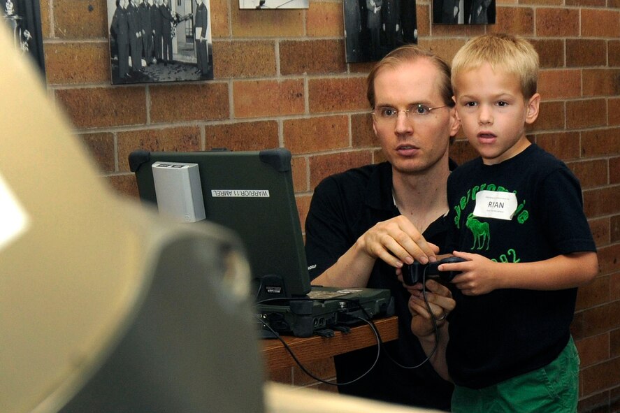 HANSCOM AIR FORCE BASE, Mass.-- Matt Brekken, iRobot Corporation representative (left), demonstrates the techniques of using the hand-held remote control to Ryan Commeau in Building 1624 during the Communications Systems Quick Reaction Capability Branch Bring Your Family to Work Day Aug. 14. Family members celebrated with branch members the Battlefield Airborne Communications Node (BACN) fleet’s 50,000 hours of service that was achieved Aug. 11. (U.S. Air Force photo Linda LaBonte Britt)