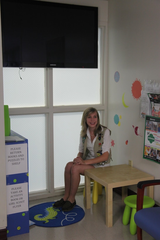 Destiny V. Oakley is sits inside the kids' corner, a new addition to the Naval Health Clinic Cherry Point pharmacy waiting area, Aug. 14. The area features reading and activity books to entertain junior patrons while they wait inside the pharmacy. Oakley, an ambassador of the Girl Scouts of the United States of America, designed the corner to give young clinic patrons something constructive to do while they wait. She earned the Girl Scouts' highest award, the Gold Award, for her efforts. 