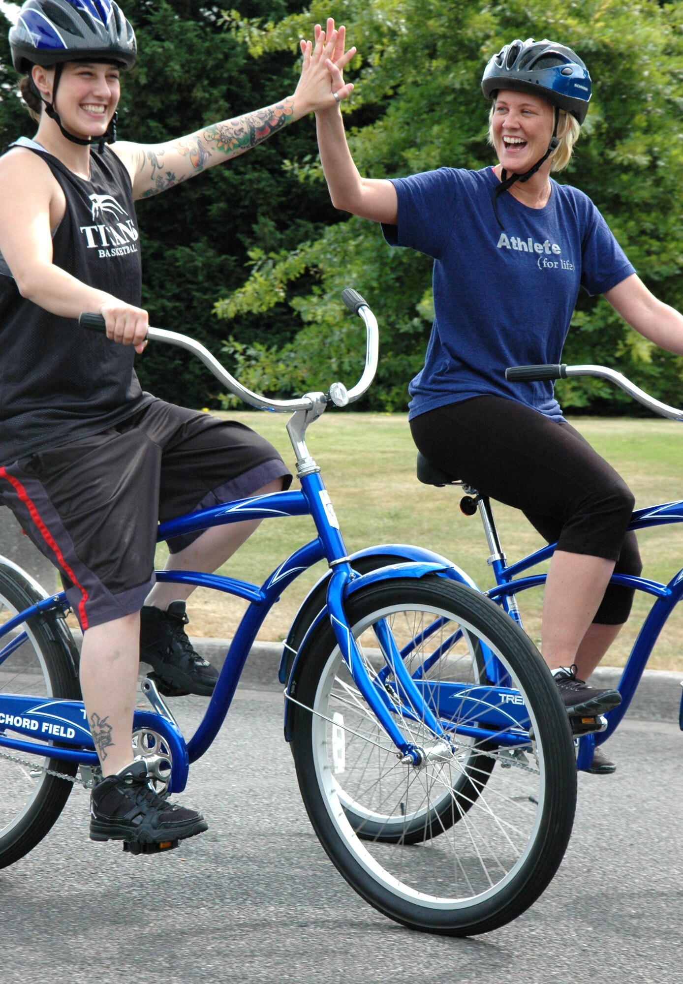 Senior Airman Laura Olson, left, joins Staff Sgt. Tara Lamson in a high-five as they start out on a lunch time ride using bikes from the McChord Blue Bike program. Olson and Lamson are with the 446th Operations Support Flight.  (U.S. Air Force Reserve photo by Sandra Pishner)
