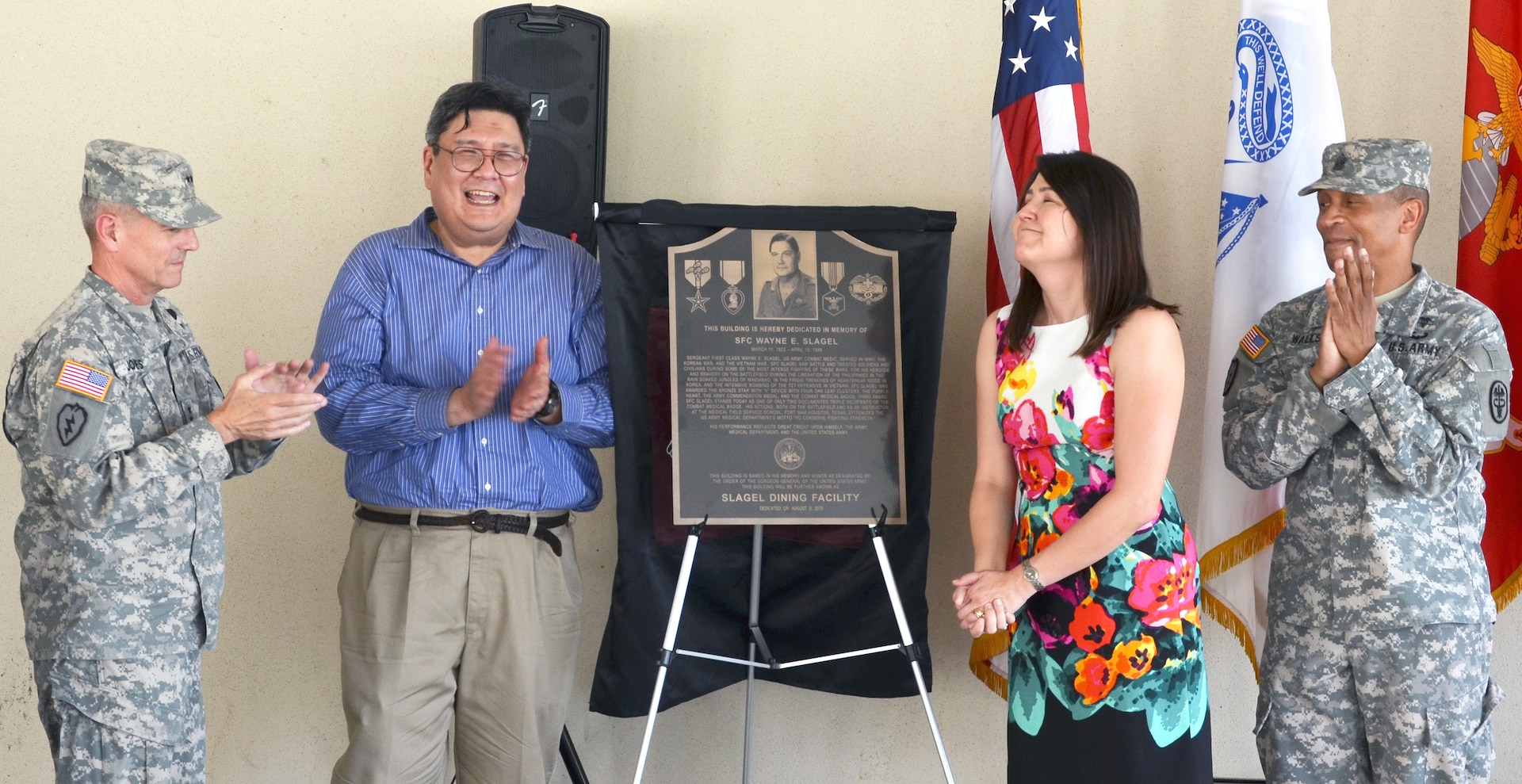 (From left) Maj. Gen. Steve Jones, Army Medical Department Center and School commanding general, is joined by David Slagel, Princess Slagel-Bucshon, and AMEDDC&S Command Sgt. Maj. Christopher Walls, as they unveil the plaque designating Dining Facility No. 3 as the Sgt. 1st Class Wayne Slagel Dining Facility during a dedication ceremony Aug. 8. The plaque hangs at the entrance of the dining facility. (Photo by Esther Garcia, U.S. Army Medical Department Center & School Public Affairs)