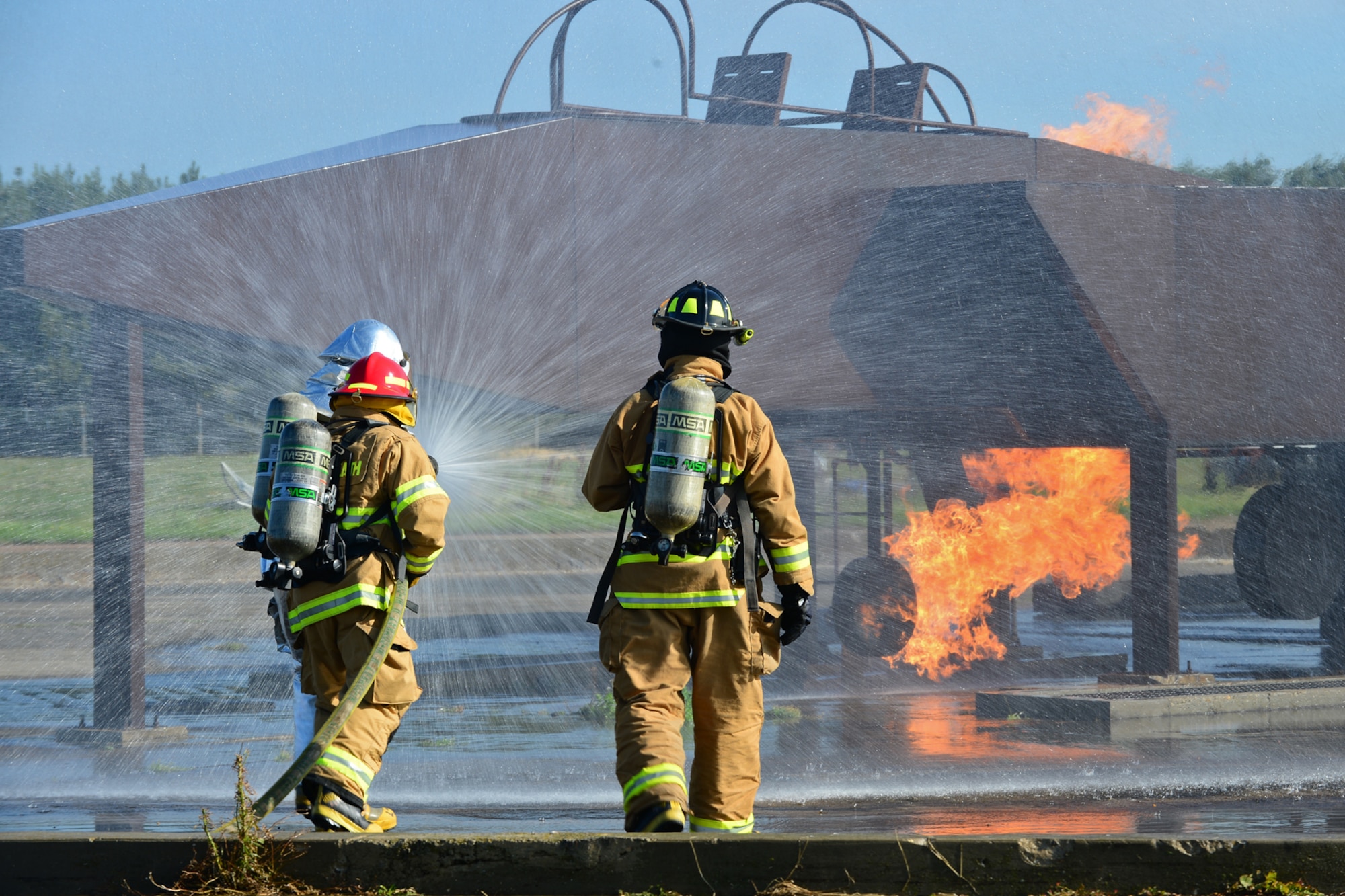 Airmen from the 48th Civil Engineer Squadron Fire Department spray a mock-up F-15 with a fire hose during live-fire training at the burn pit on Royal Air Force Lakenheath, England, Aug. 20, 2013. Live-fire training is mandatory for firefighters to complete twice a year. The training ensures firefighters are able to perform required core tasks in the event of an aircraft fire. (U.S. Air Force photo by Airman 1st Class Dana J. Butler/Released)