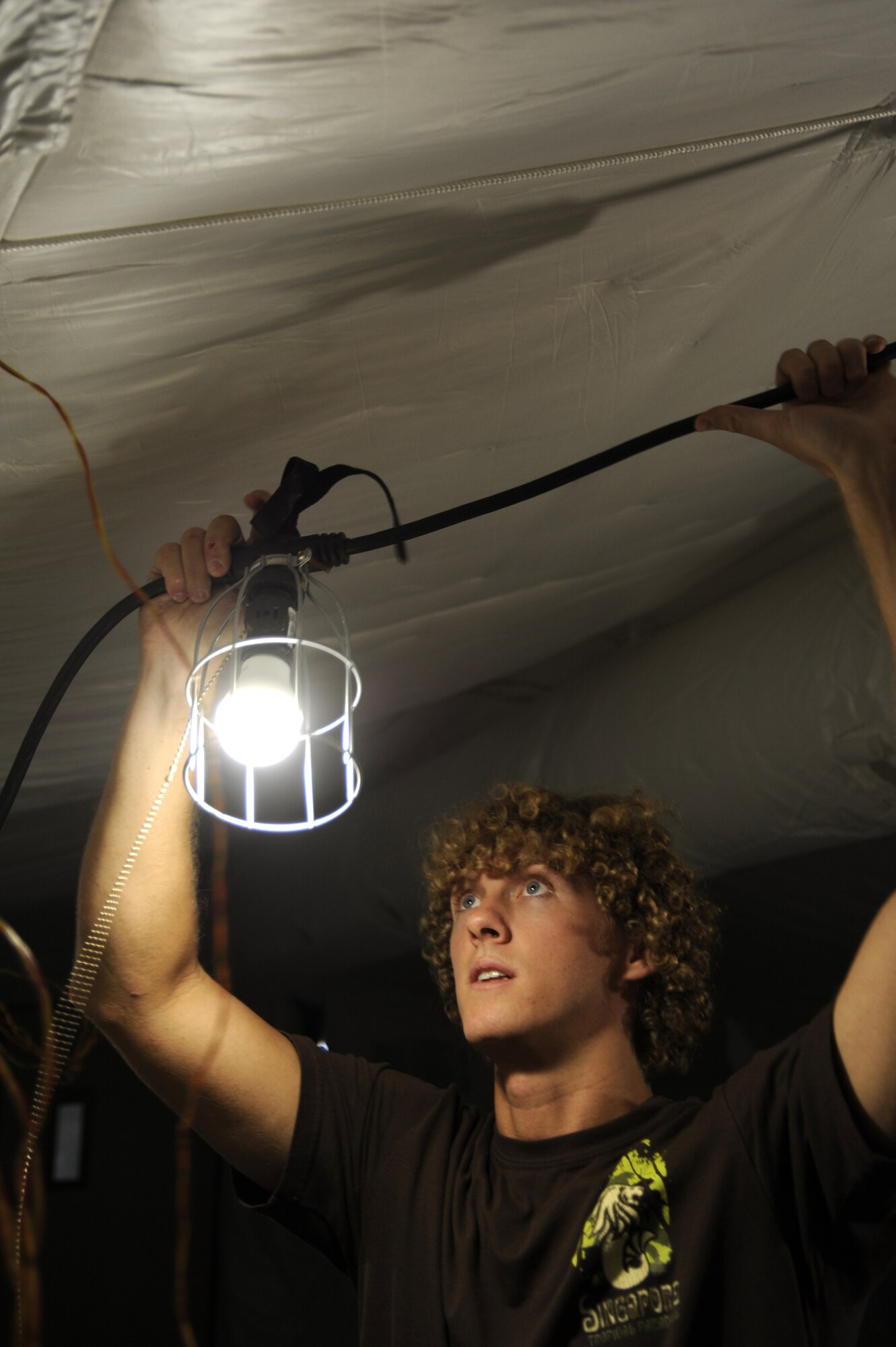 Chris Church, a member of the Air Force Civil Engineer Center, finds the right place to hang an energy saving light here, Aug. 12, 2013. Chris is using these lights to monitor the energy used during the testing phase of this project. This project is testing new energy-efficient technologies to reduce the amount of energy for future operations. Chris is deployed out of Panama City Beach, Fla. (U.S. Air Force photo by Master Sgt. Christopher A. Campbell)