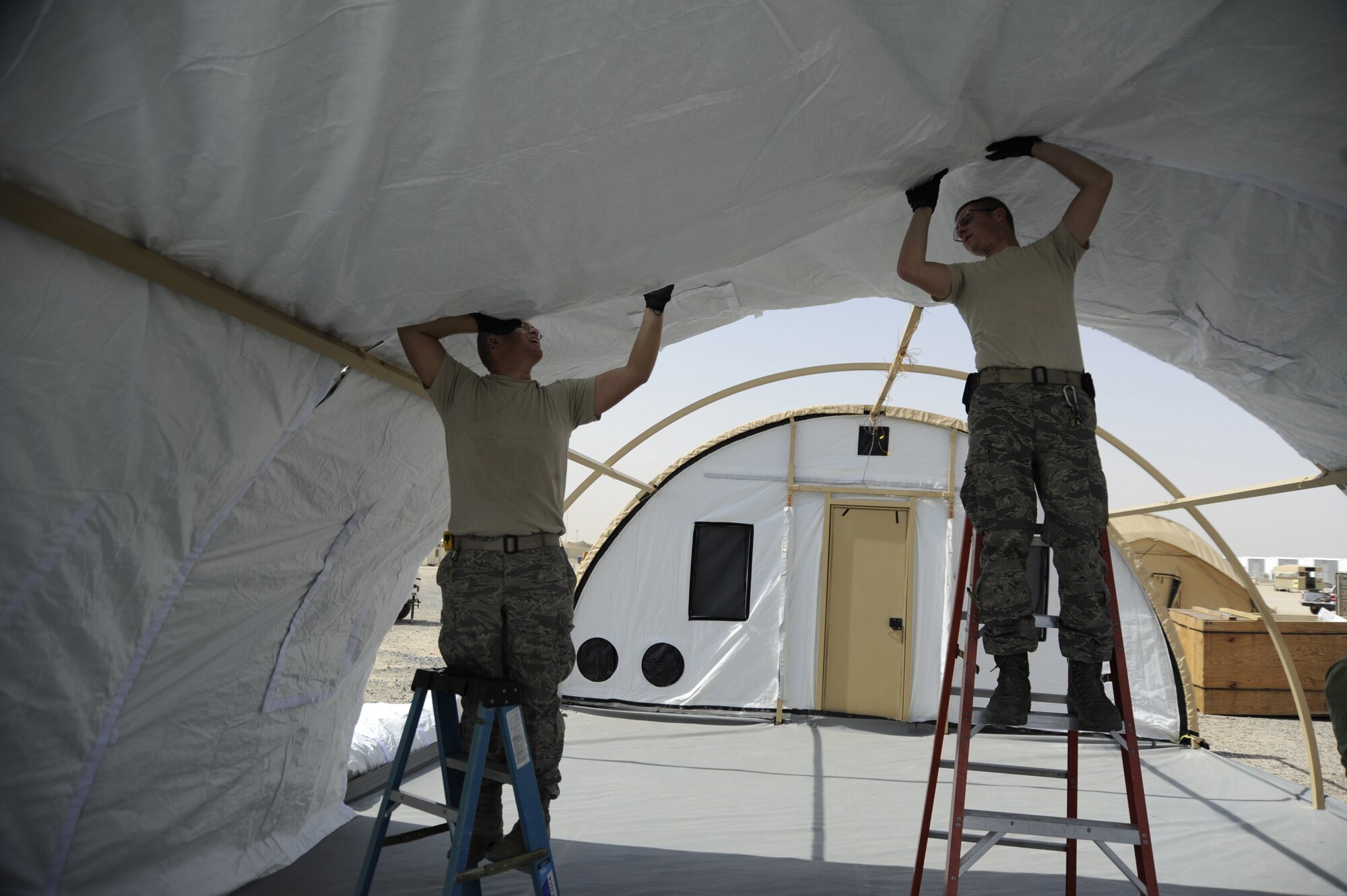 (From left to right) Tech. Sgt. Quentin Greiner and Staff Sgt. Casey Nowicki, 386th Expeditionary Civil Engineer Squadron, structures flight, work together to put up a tent here, Aug. 6, 2013. They are fastening the insulation lining of the tent before putting the cover on it. This lining is just one new technology being tested here. They are working together with members of the Air Force Civil Engineer Center testing new energy-efficient technologies to reduce the amount of energy for future operations. Both members are deployed out of the 110th Airlift Wing, Battle Creek, Mich., Air National Guard unit. (U.S. Air Force photo by Master Sgt. Christopher A. Campbell)