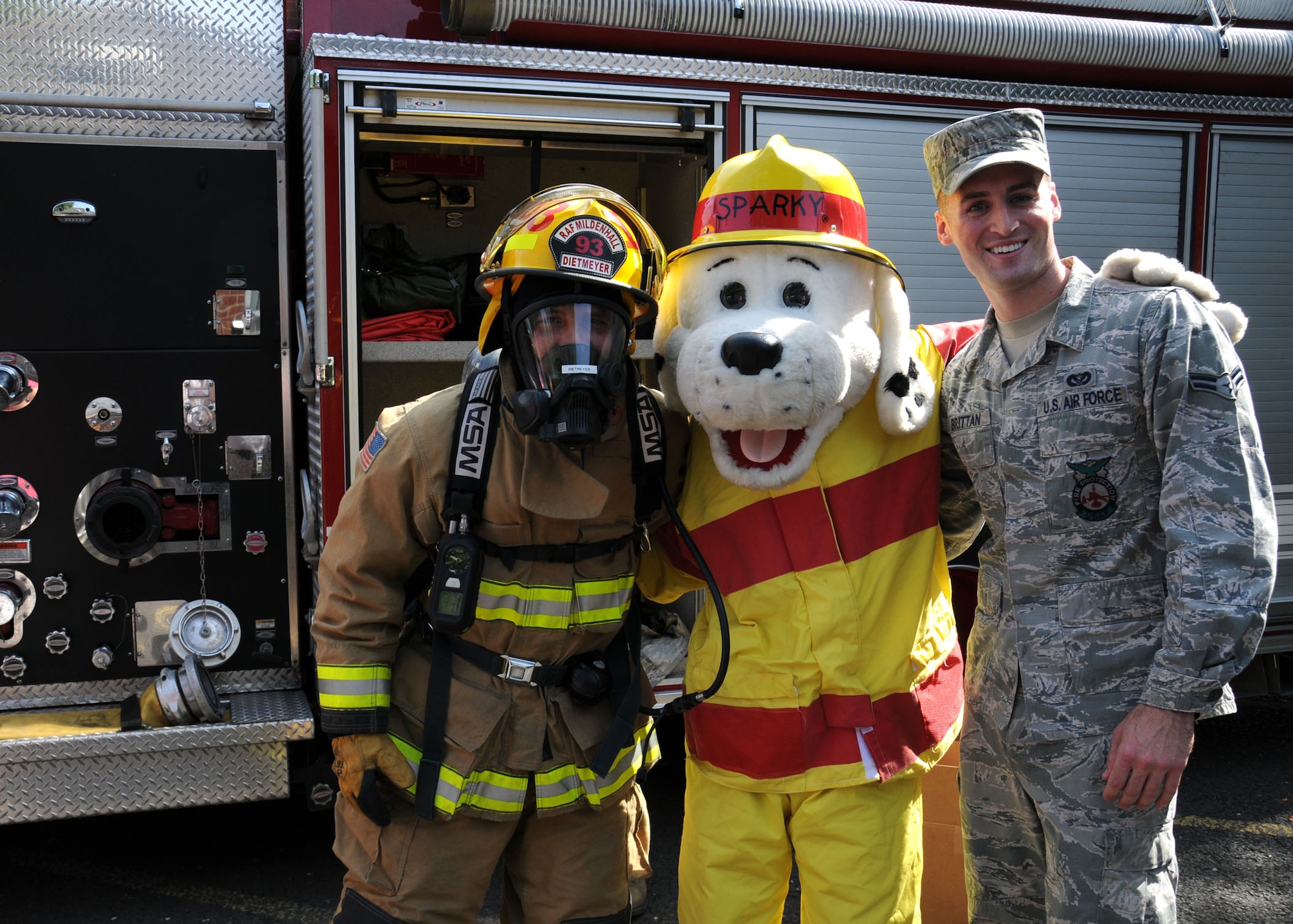 U.S. Air Force Airman 1st Class Jacob Dietmeyer, left, 100th Civil Engineer Squadron Fire Department firefighter from Gurnee, Ill.; “Sparky,” 100th CES Fire Department mascot; and U.S. Air Force Airman 1st Class Kevin Brittan, 100th CES Fire Department firefighter from Lindenhurst, N.Y., pose for a photograph following a book-reading session Aug. 21, 2013, at the library on RAF Mildenhall, England. The firefighters taught the children firefighters are to be trusted and not feared. The firefighters hoped that by children seeing them as real people, in the event of an emergency children would not panic and would follow firefighters’ instructions to safety. (U.S. Air Force photo by Gina Randall/Released)