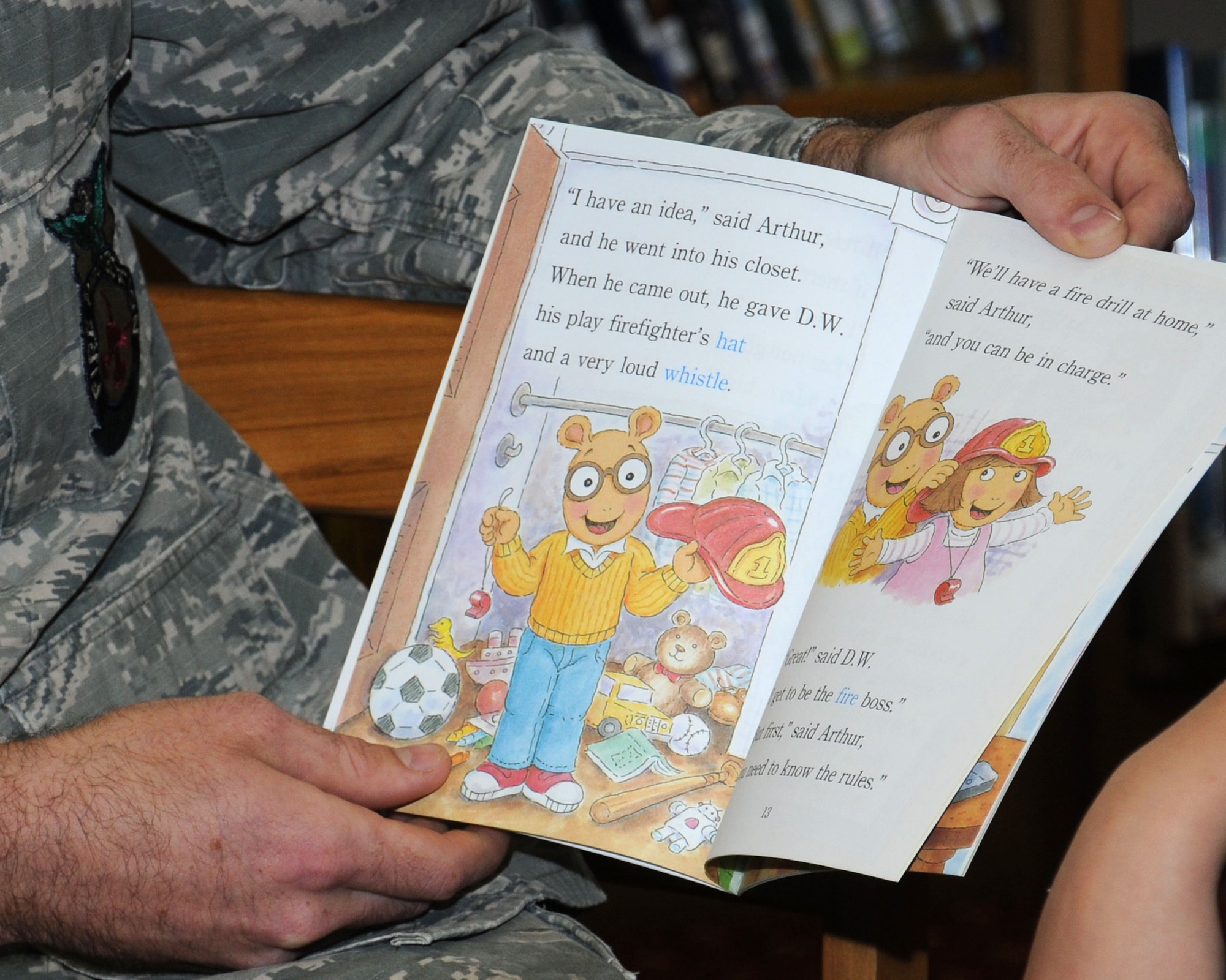U.S. Air Force Airman 1st Class Kevin Brittan, 100th Civil Engineer Squadron Fire Department firefighter from Lindenhurst, N.Y., reads a book with a fire safety theme to Team Mildenhall children Aug. 21, 2013, at the library on RAF Mildenhall, England. Brittan read two books to the children to give the messages of fire prevention and safety while using characters with which the children are familiar. The children also took part in a fire safety-themed arts and crafts session. (U.S. Air Force photo by Gina Randall/Released)